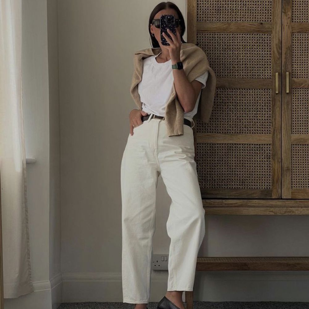 woman wearing cream jeans with a white tshirt with a beige sweater draped on her shoulders