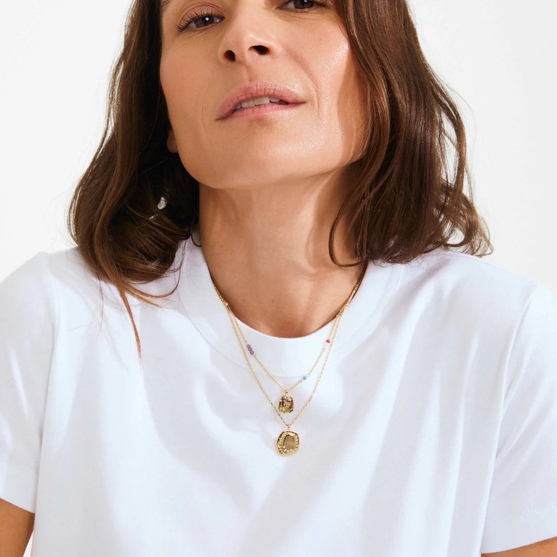 Woman wearing a white t-shirt and gold necklaces on a plain background