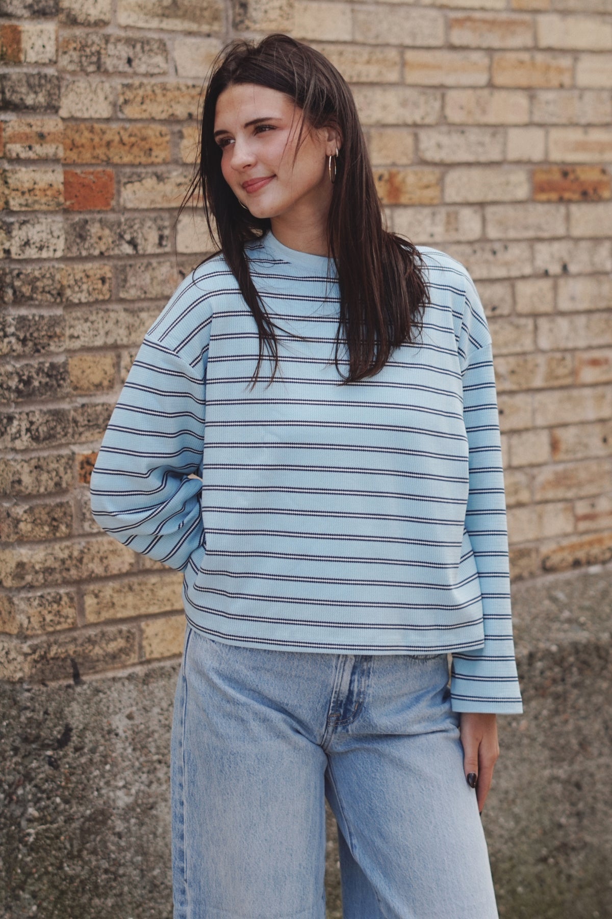 A woman wearing a light blue and white striped long-sleeve top with light-wash blue jeanS.