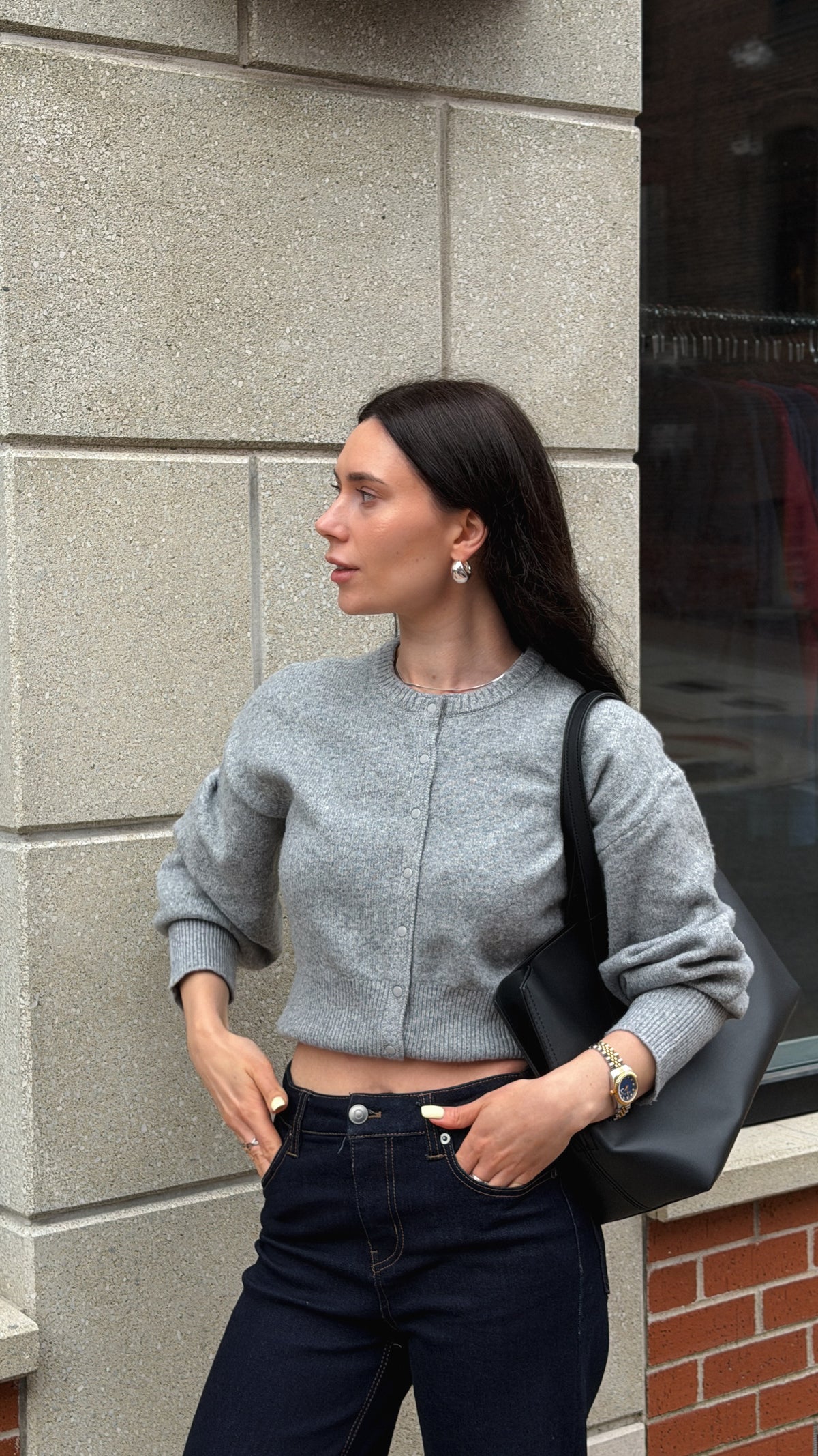 Woman wearing a cropped grey crewneck sweater with dark denim and a black shoulder bag.
