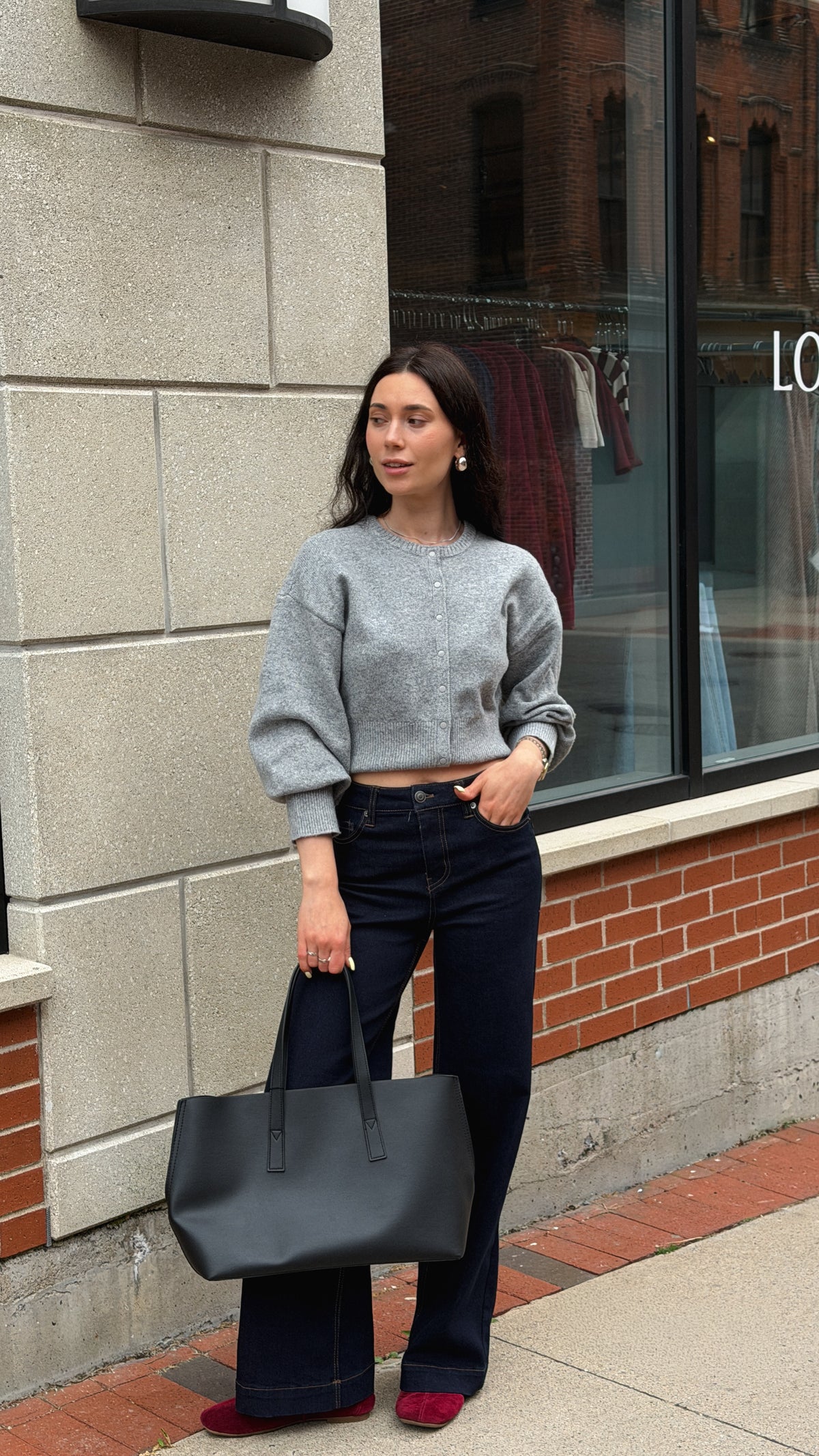 Woman wearing a cropped grey crewneck sweater with dark denim and a black shoulder bag.