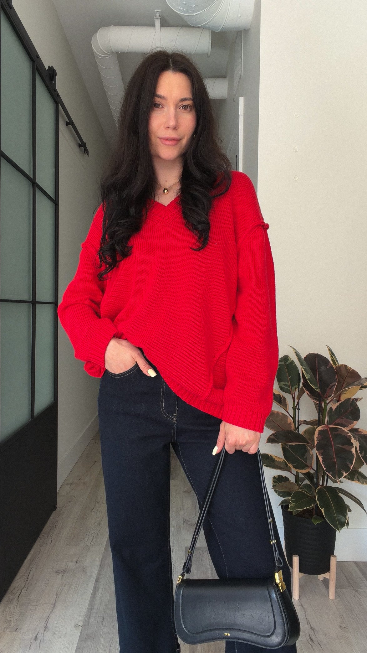 Woman wearing a bright red V-neck knit sweater with dark wide-leg jeans and a black shoulder bag.
