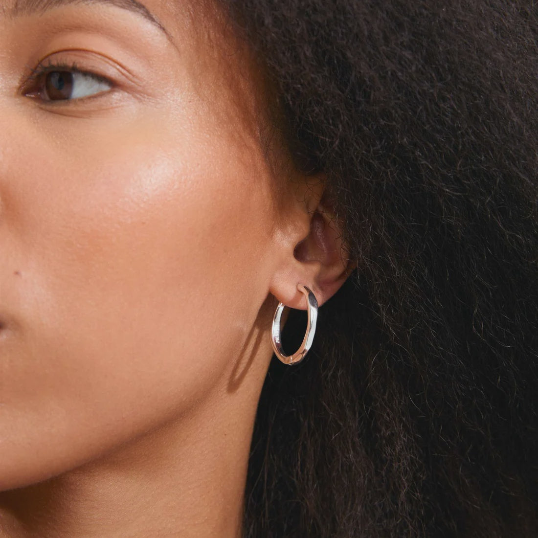 A close-up of a model's ear wearing a polished silver-tone hoop earring.
