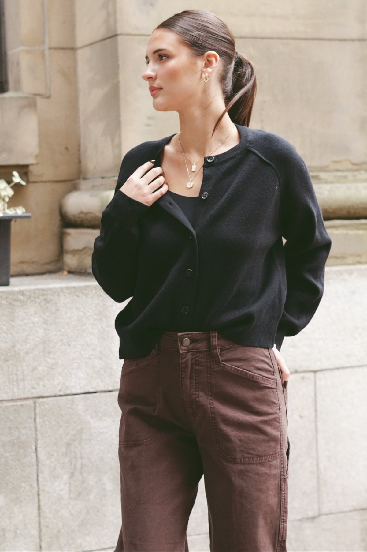 A woman wearing a black knit button-front cardigan and brown corduroy pants
