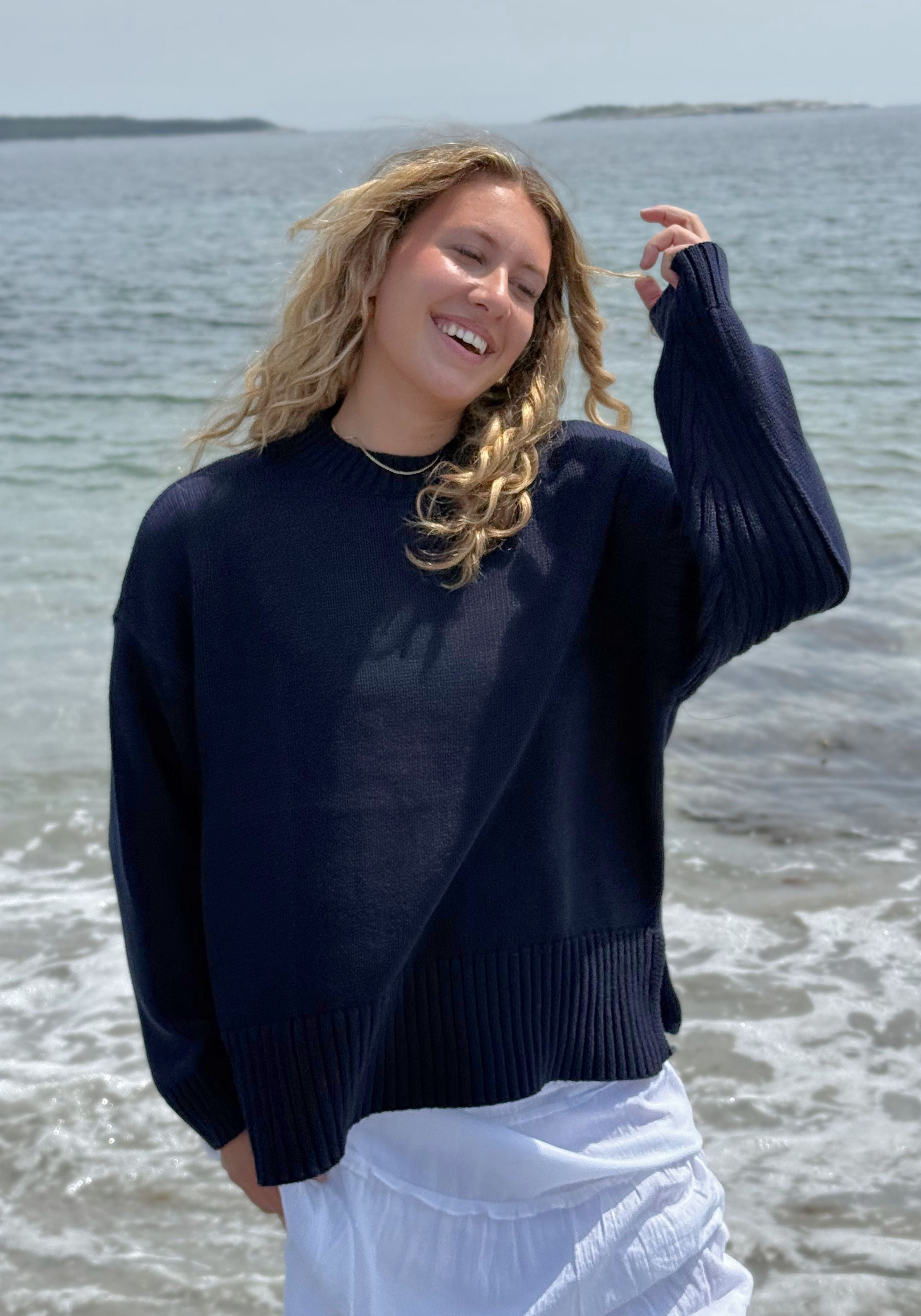 A woman wearing an oversized dark navy knit sweater and white skirt.