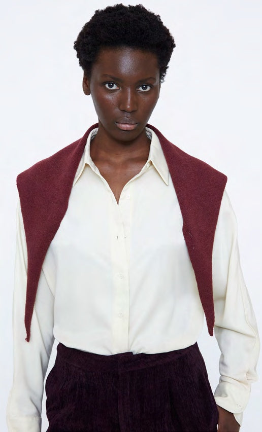 A model wearing a cream button-up shirt with a burgundy knit collar and matching burgundy corduroy trousers, photographed against a plain white background.