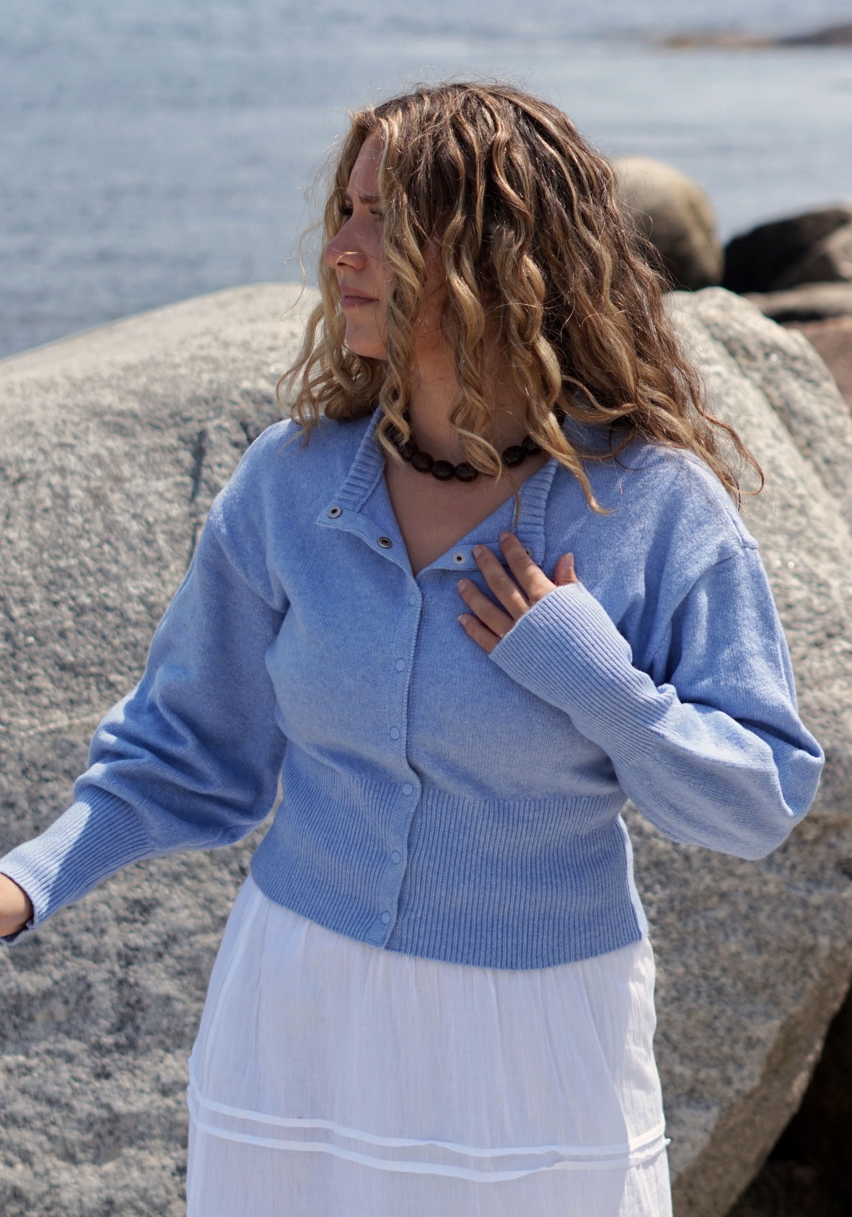 A woman wearing a light blue ribbed knit cardigan over a white skirt.