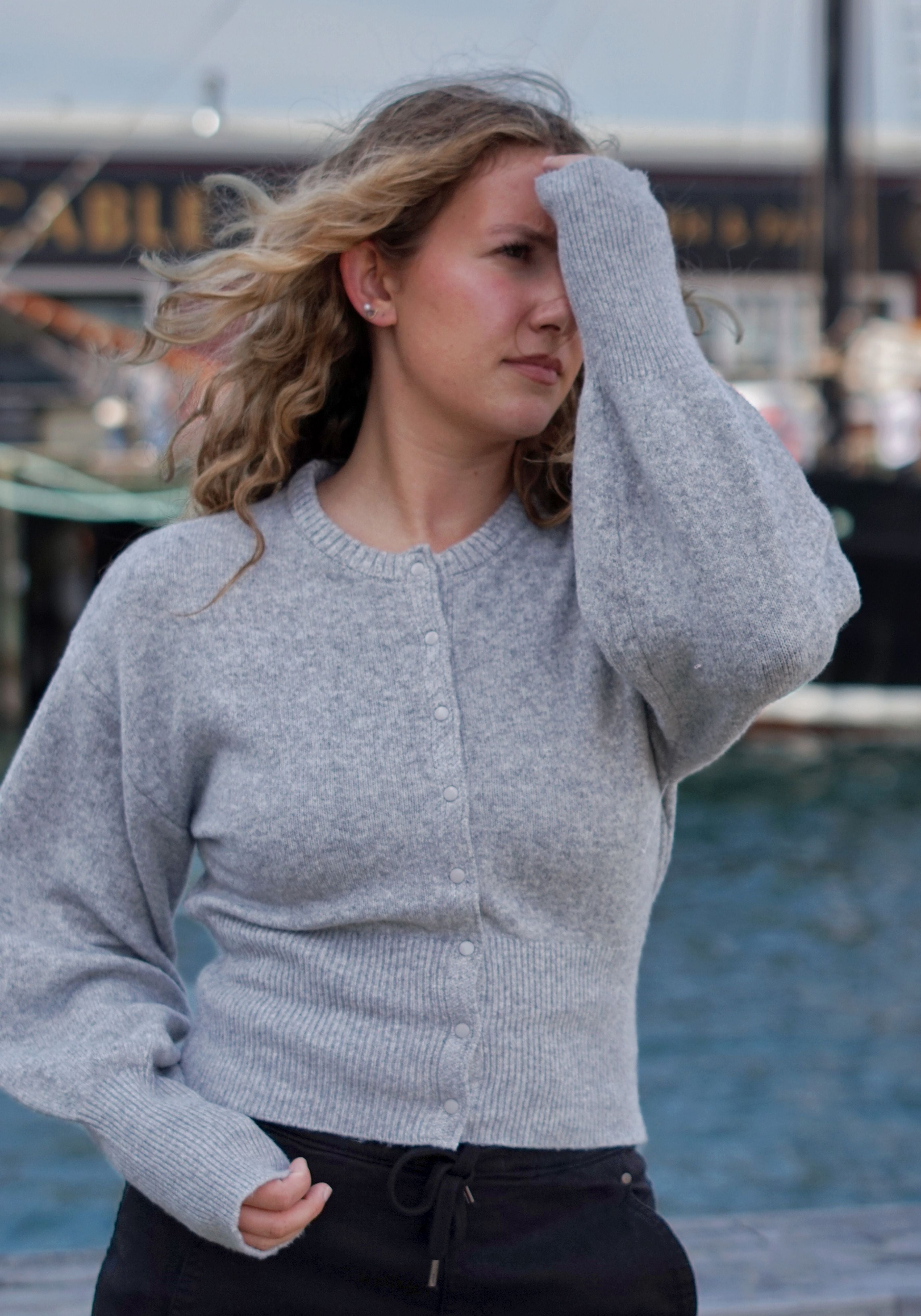 A woman wearing a light gray ribbed knit cardigan sweater with long sleeves and a button front, standing outdoors.