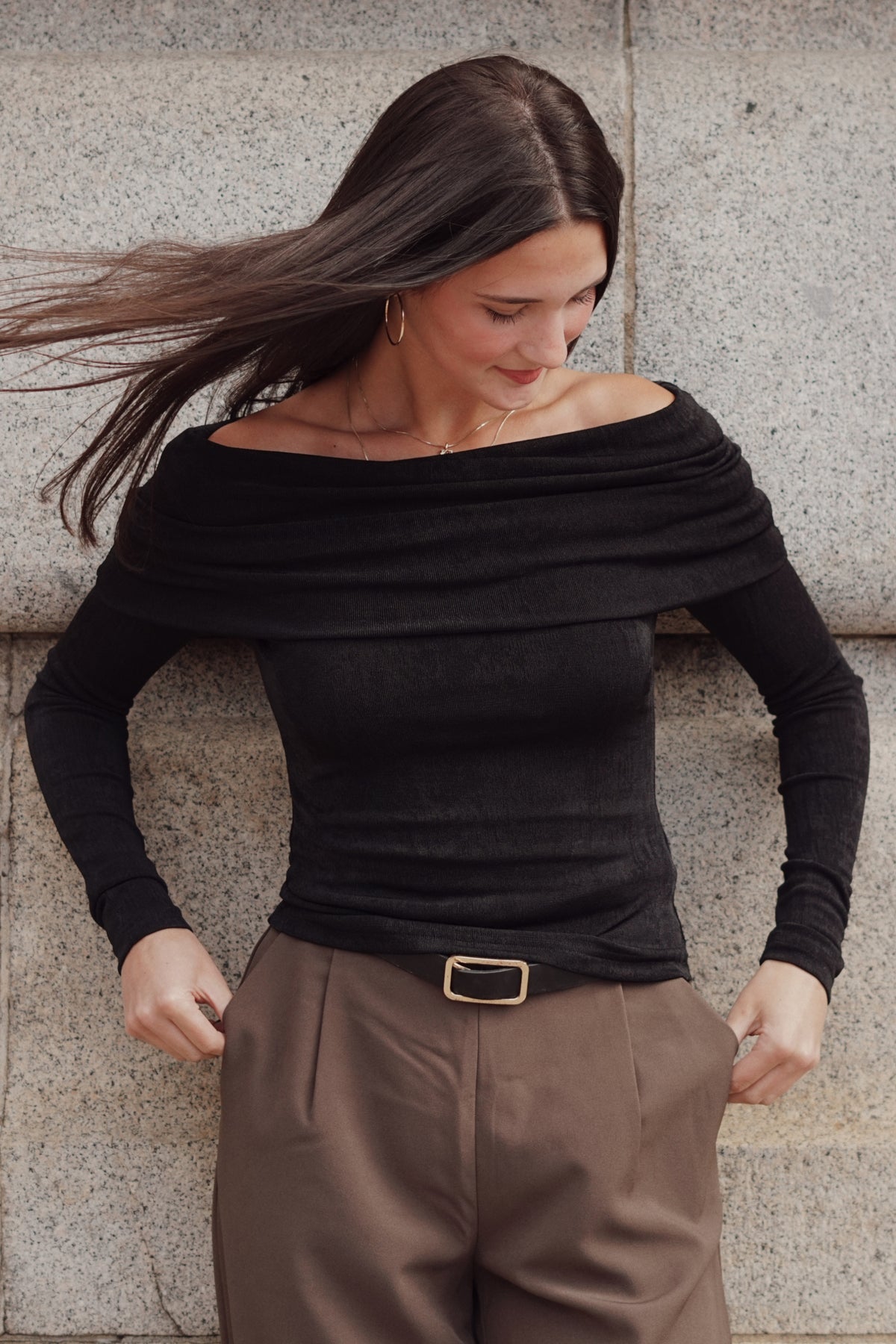 A woman wearing a black off-the-shoulder long-sleeve top and brown trousers.
