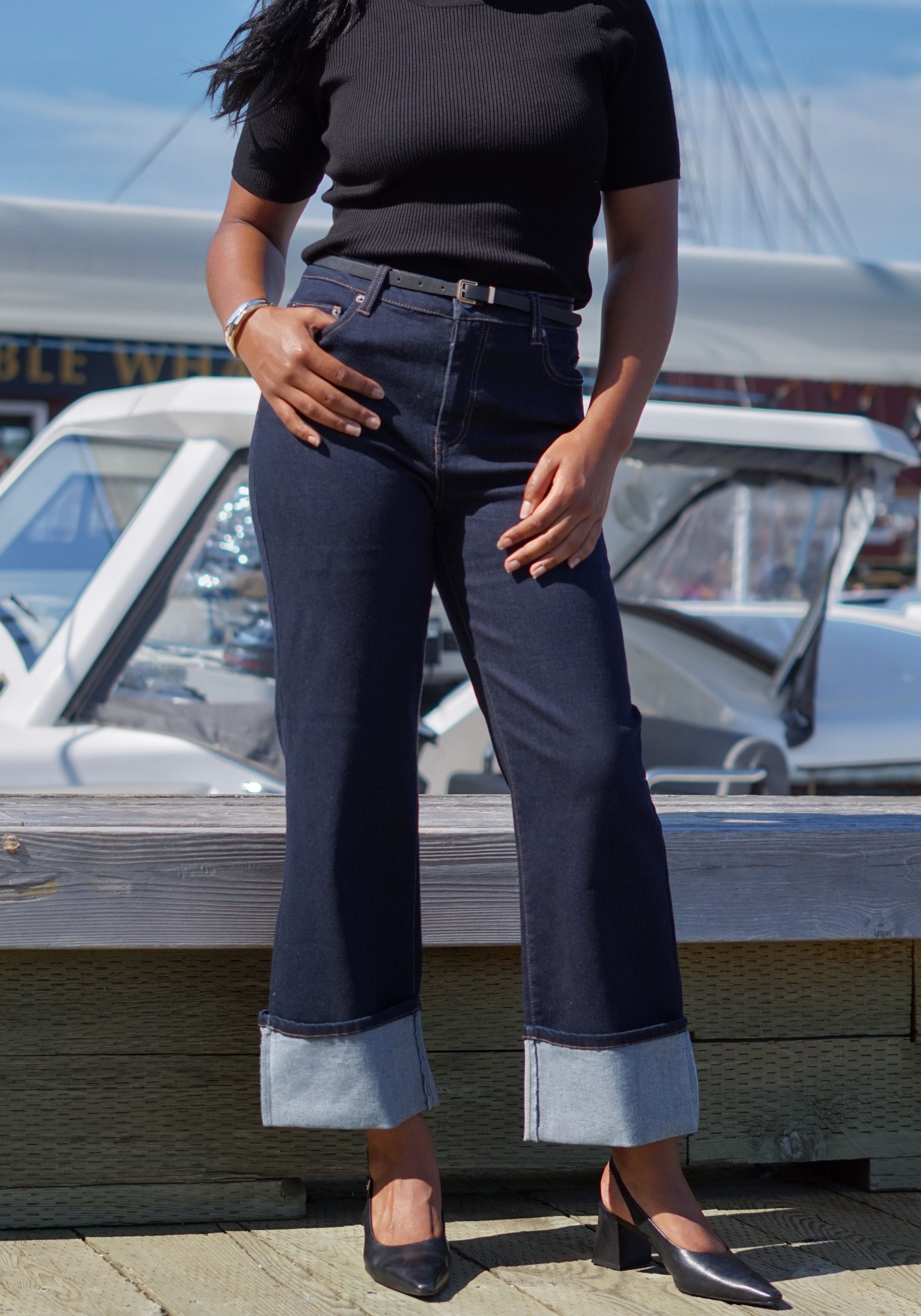A person wearing dark blue wide-leg cuffed jeans with a black ribbed short-sleeve top and black heels.