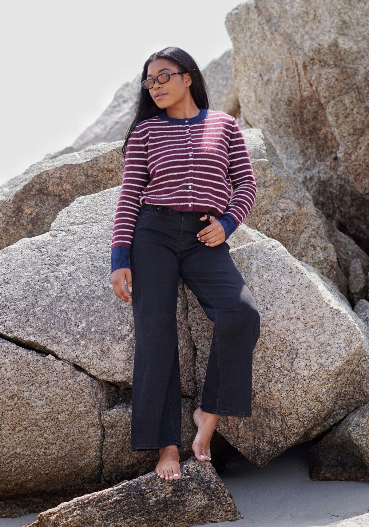 A woman wearing a burgundy and navy striped long-sleeve button-up cardigan and dark navy wide-leg pants.