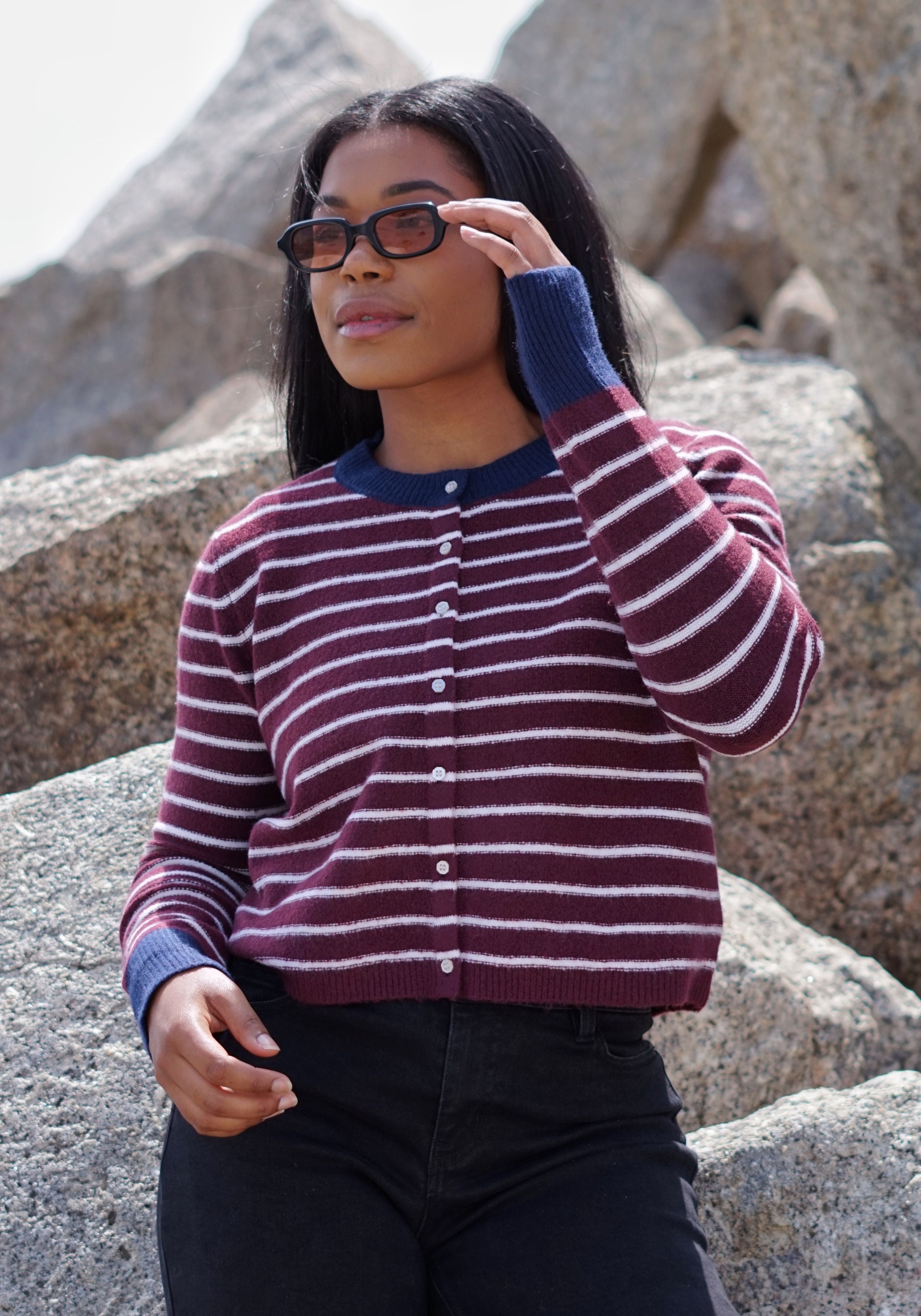 A woman wearing a burgundy and white striped knit cardigan with navy blue trim.