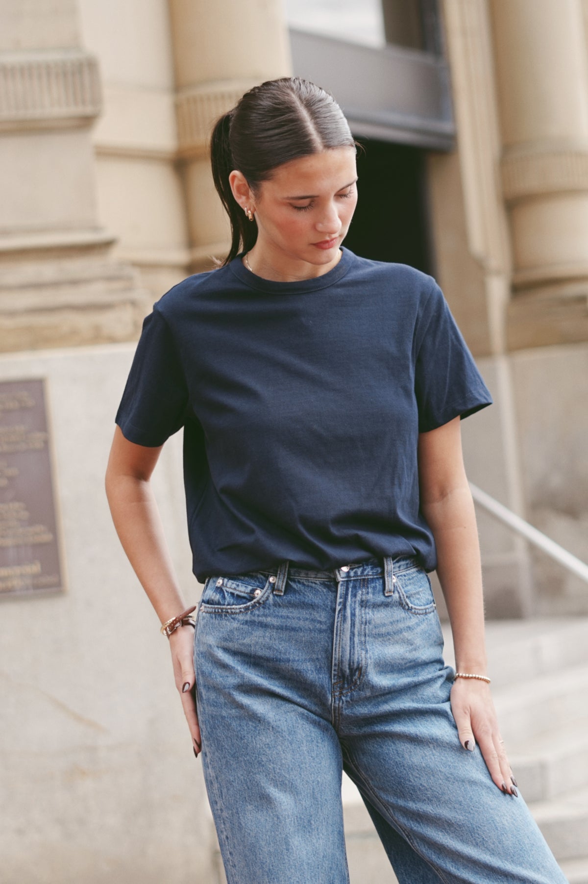 A woman wearing a dark navy blue short-sleeve crewneck t-shirt and light-wash blue jeans