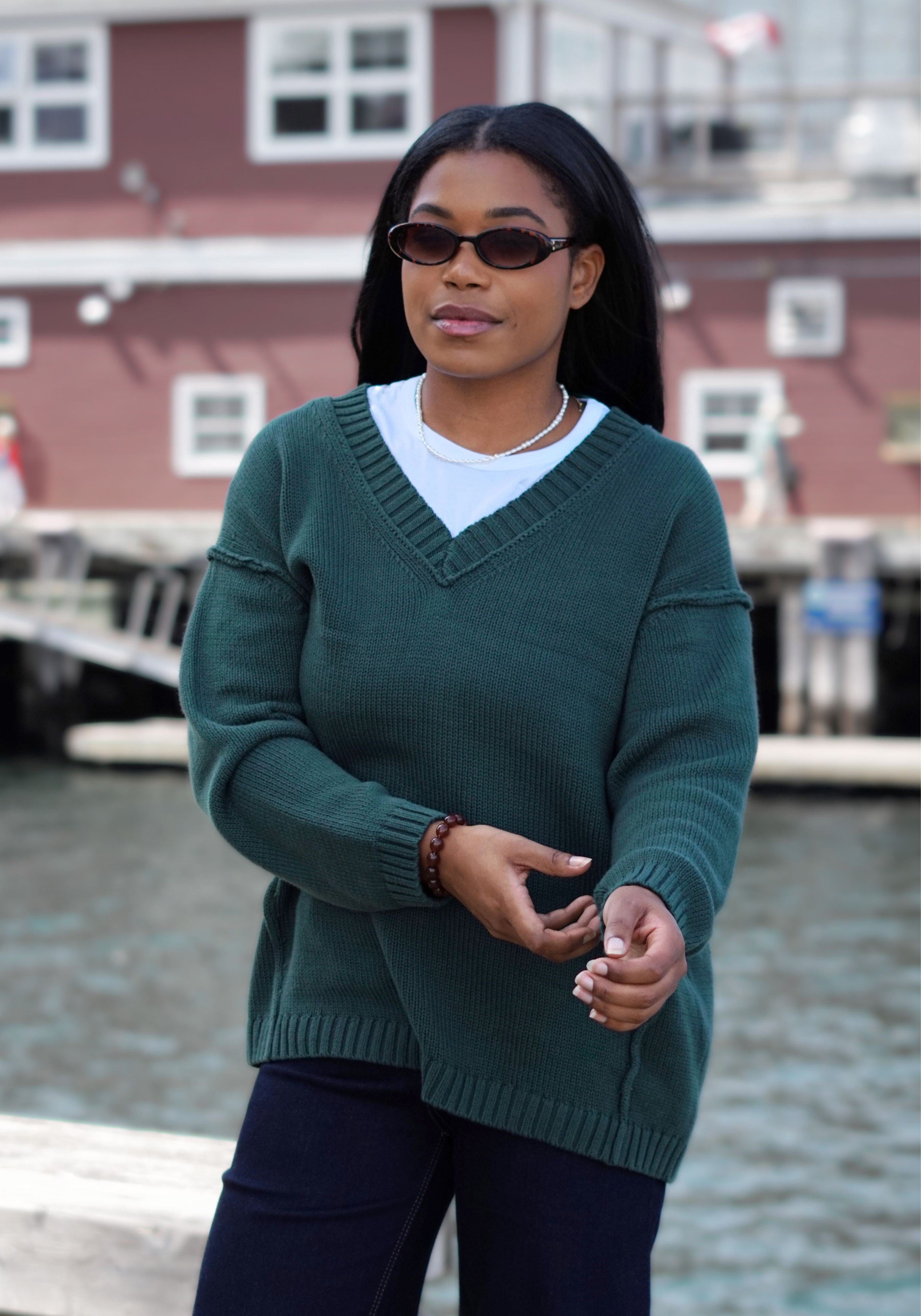 A woman wearing a dark green ribbed V-neck sweater over a white t-shirt and dark pants.