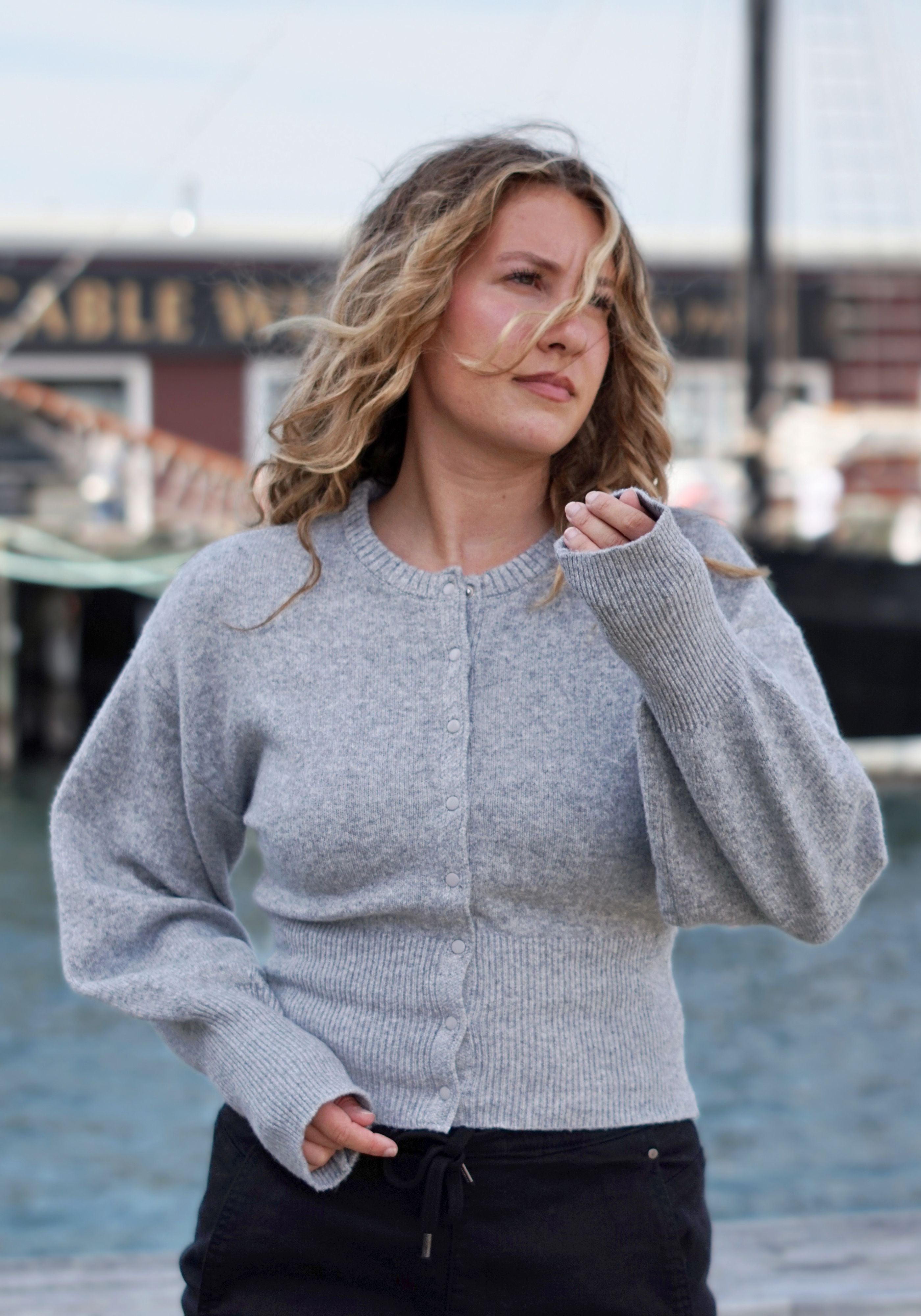 A woman wearing a light gray ribbed knit cardigan sweater with a button-up front.