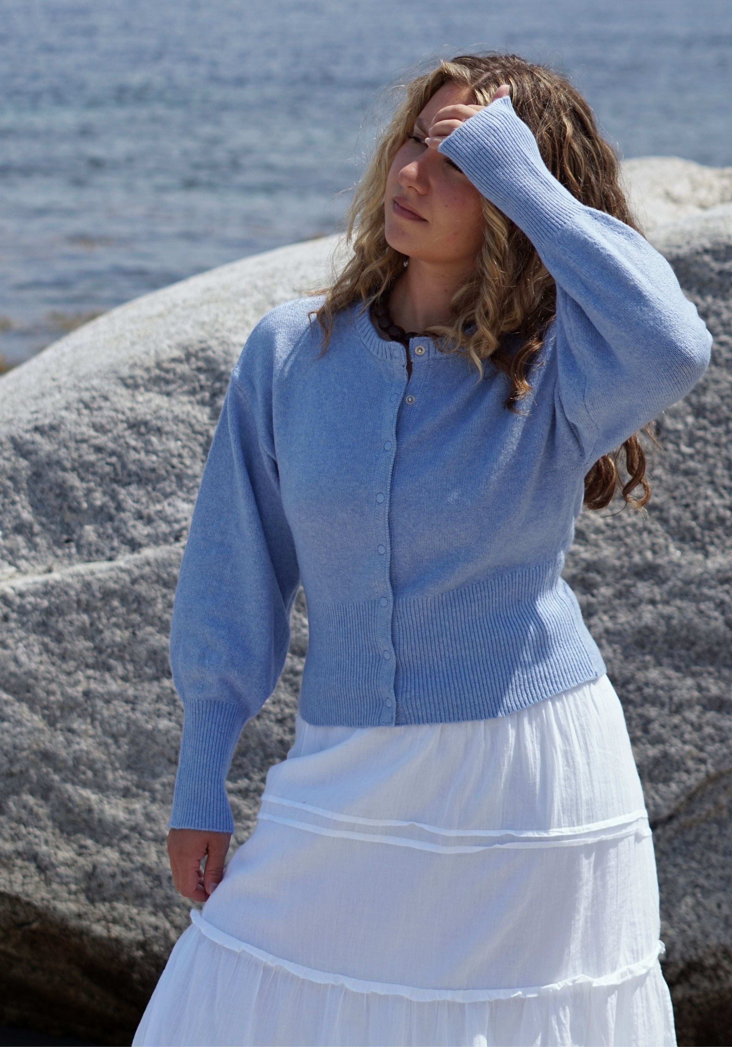 A woman wearing a light blue knit cardigan and a white tiered skirt.