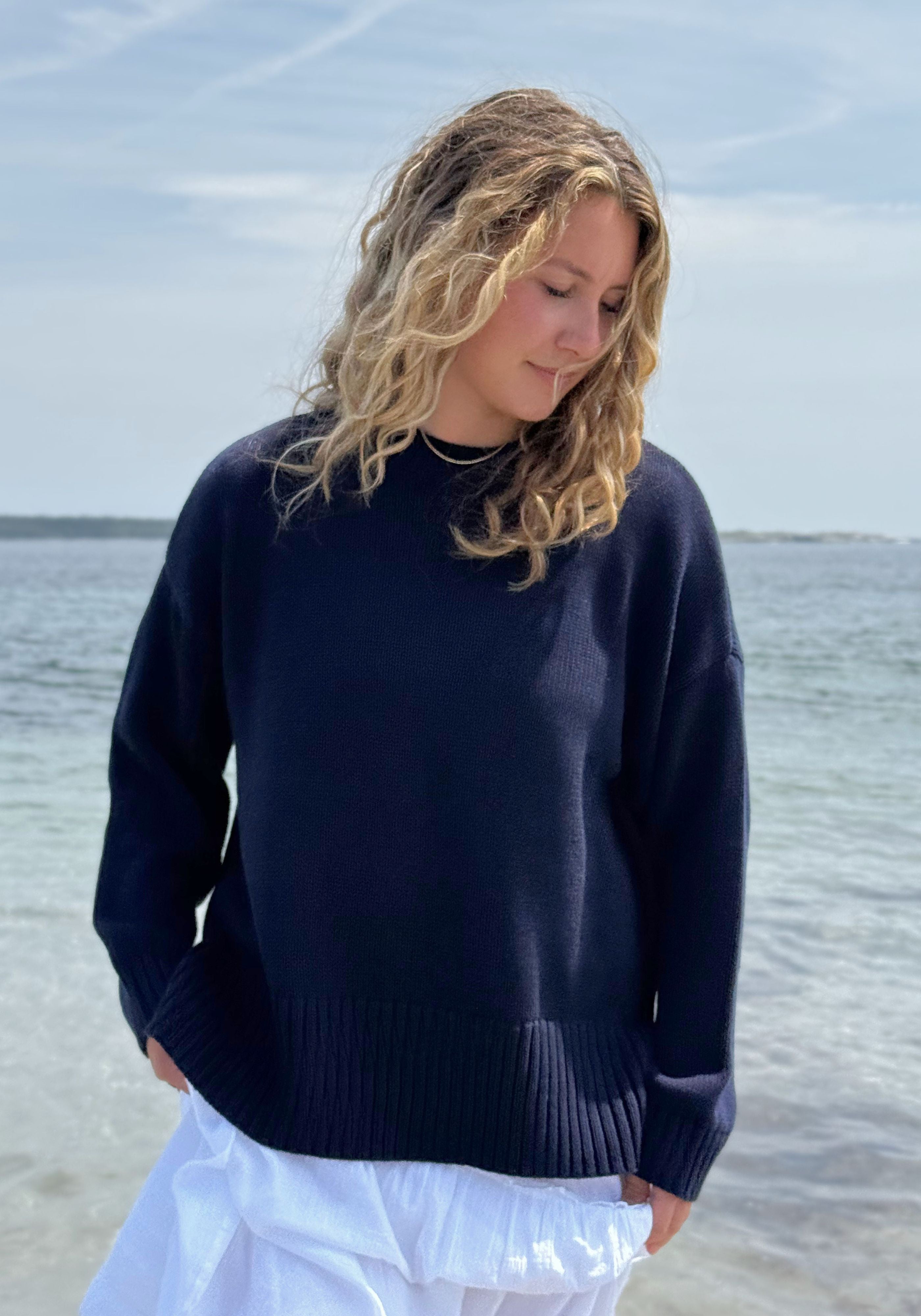 A woman wearing a dark navy blue knit sweater and a white skirt, standing outdoors.