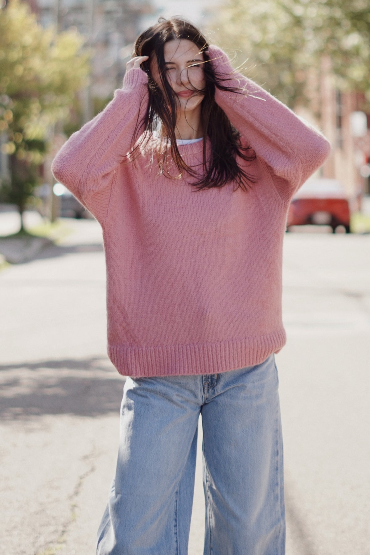A woman wearing a fuzzy, oversized dusty pink knit sweater and light blue wide-leg jeans.