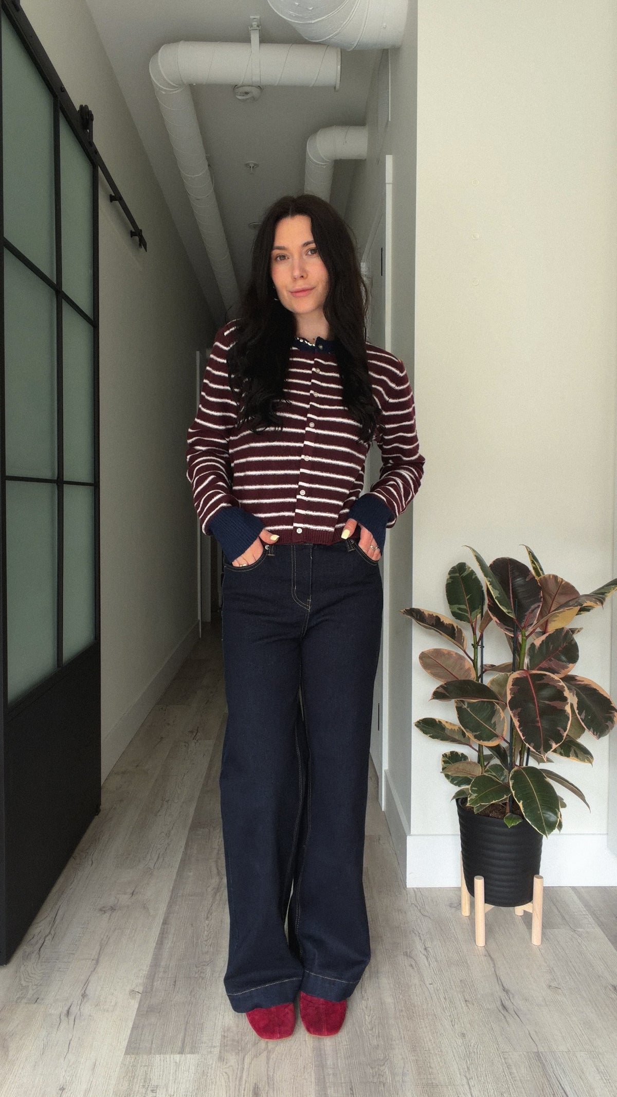 Woman wearing a burgundy and white striped cardigan with dark wide-leg jeans.