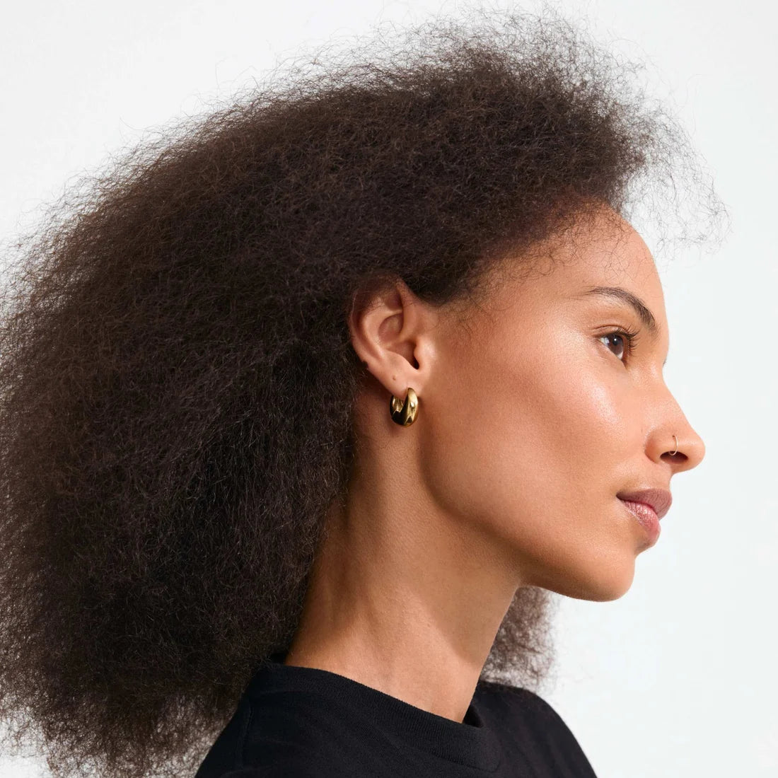 A close-up of a person's ear wearing a small polished gold hoop earring.