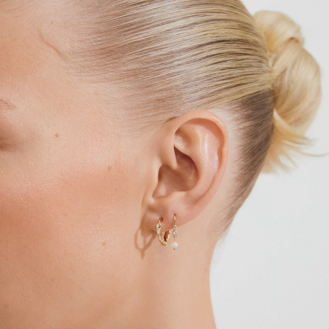 A close-up side profile of a woman's head showing a small gold hoop earring with a tiny clear crystal accent on her earlobe.