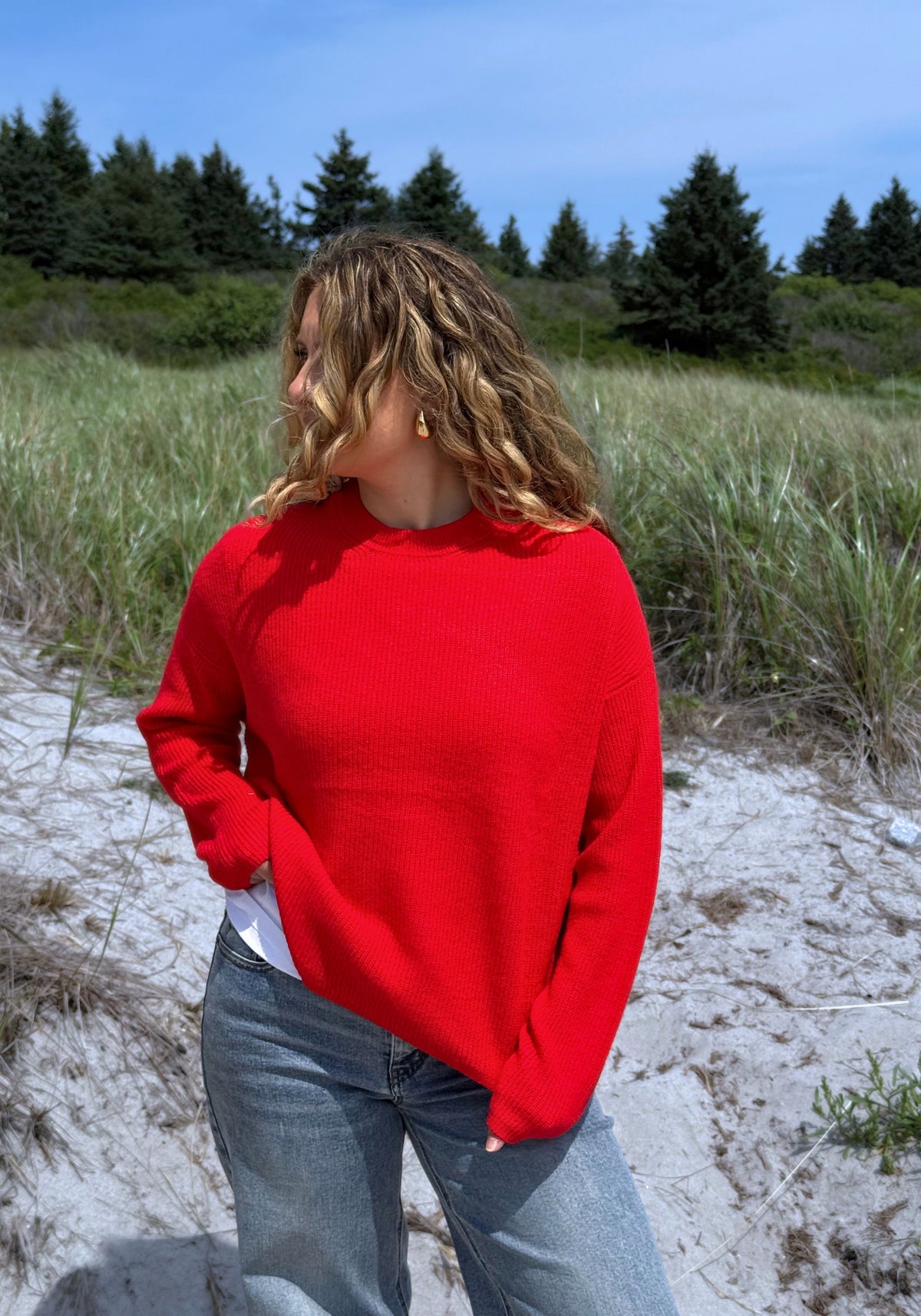 A woman wearing a bright red knit crewneck sweater and light blue jeans.