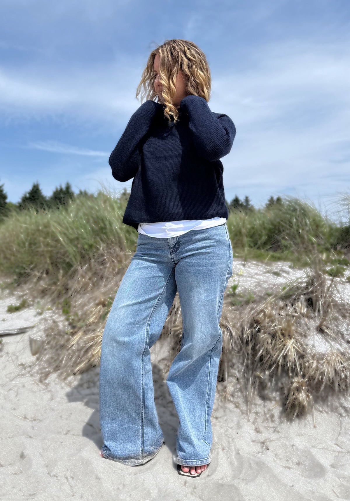 A woman wearing a dark navy blue knit sweate with light-wash wide-leg blue jeans.