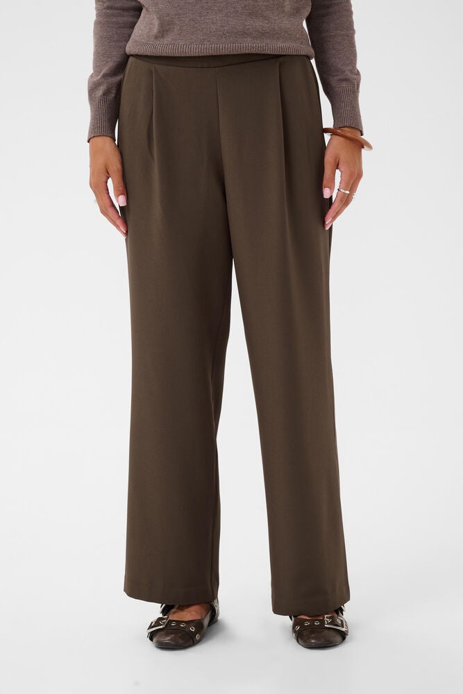 A person wearing dark brown wide-leg trousers with a matching knit top and dark flat shoes, shown from the waist down against a plain light gray studio background.
