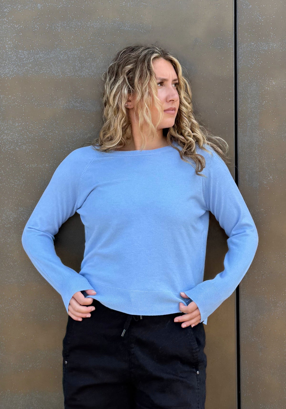 A woman wearing a light blue long-sleeve boat-neck top and black pants.