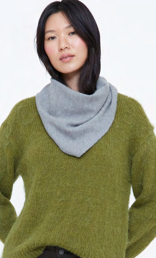 A woman wearing a chunky olive green knit sweater and a light gray cowl neck scarf, photographed against a clean white background.