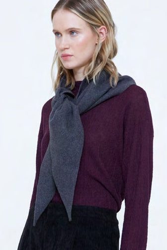 A woman modeling a dark plum long-sleeve knit top with a draped dark gray scarf, paired with black corduroy trousers, against a plain white studio background.