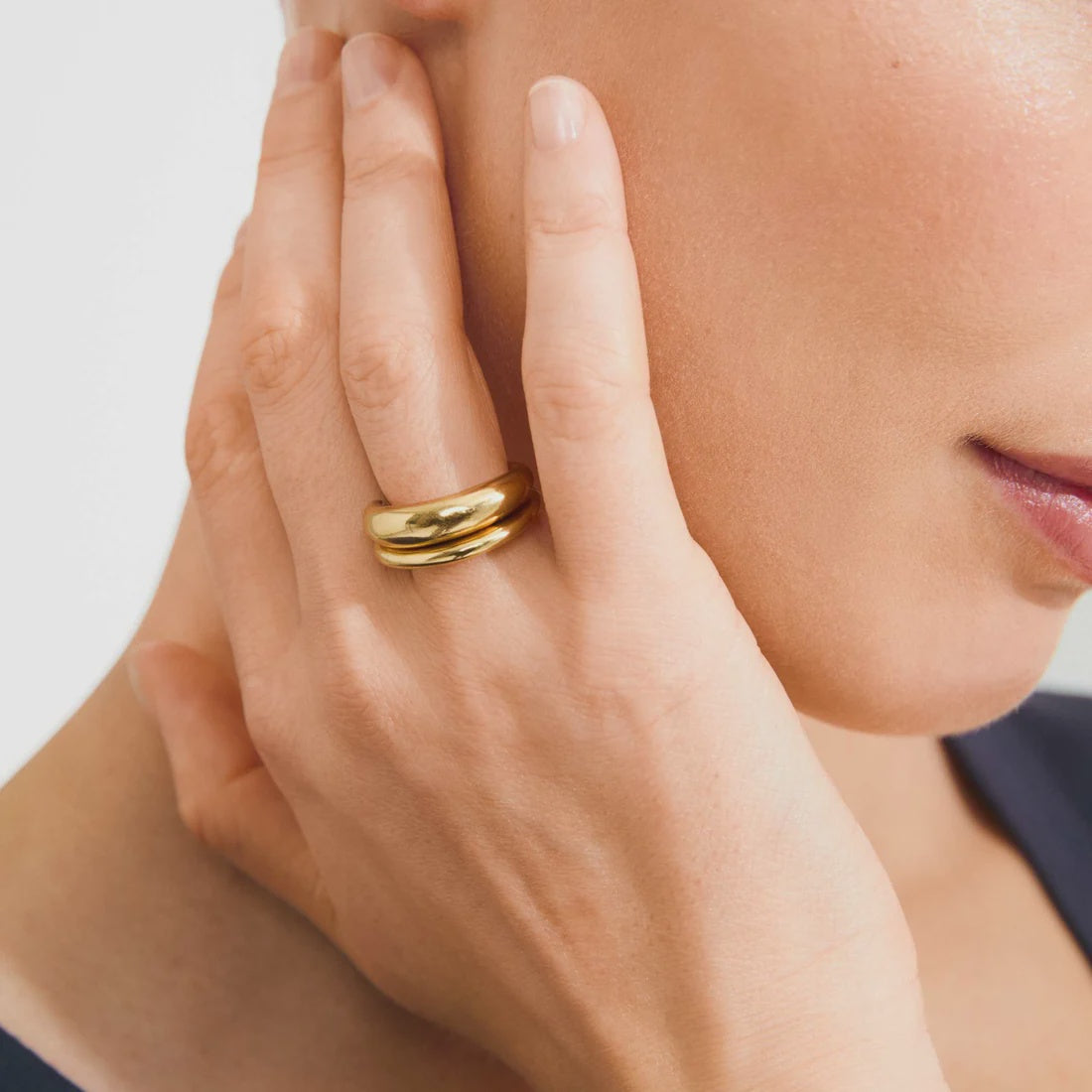 Close-up of a hand wearing a gold ring on a neutral background