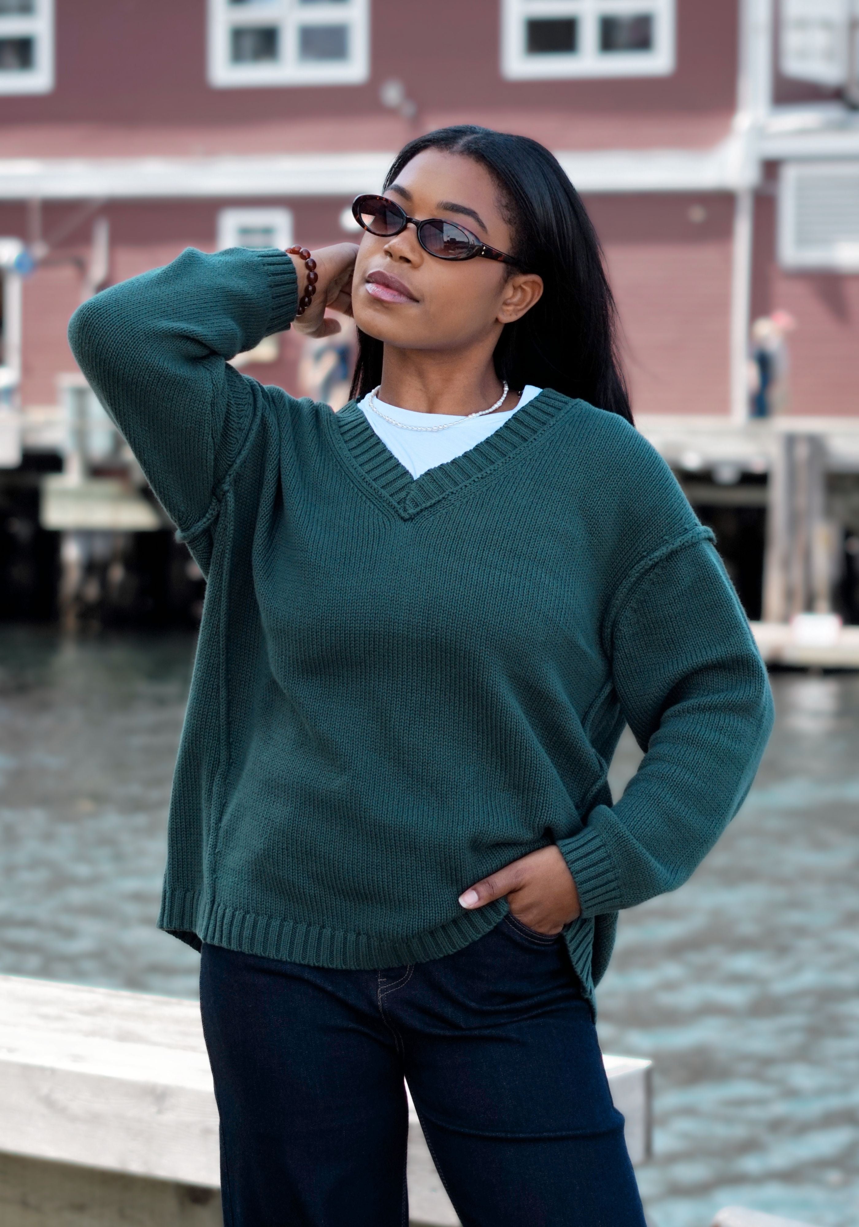 A woman wearing an oversized dark green v-neck knit sweater over a white t-shirt and dark jeans.