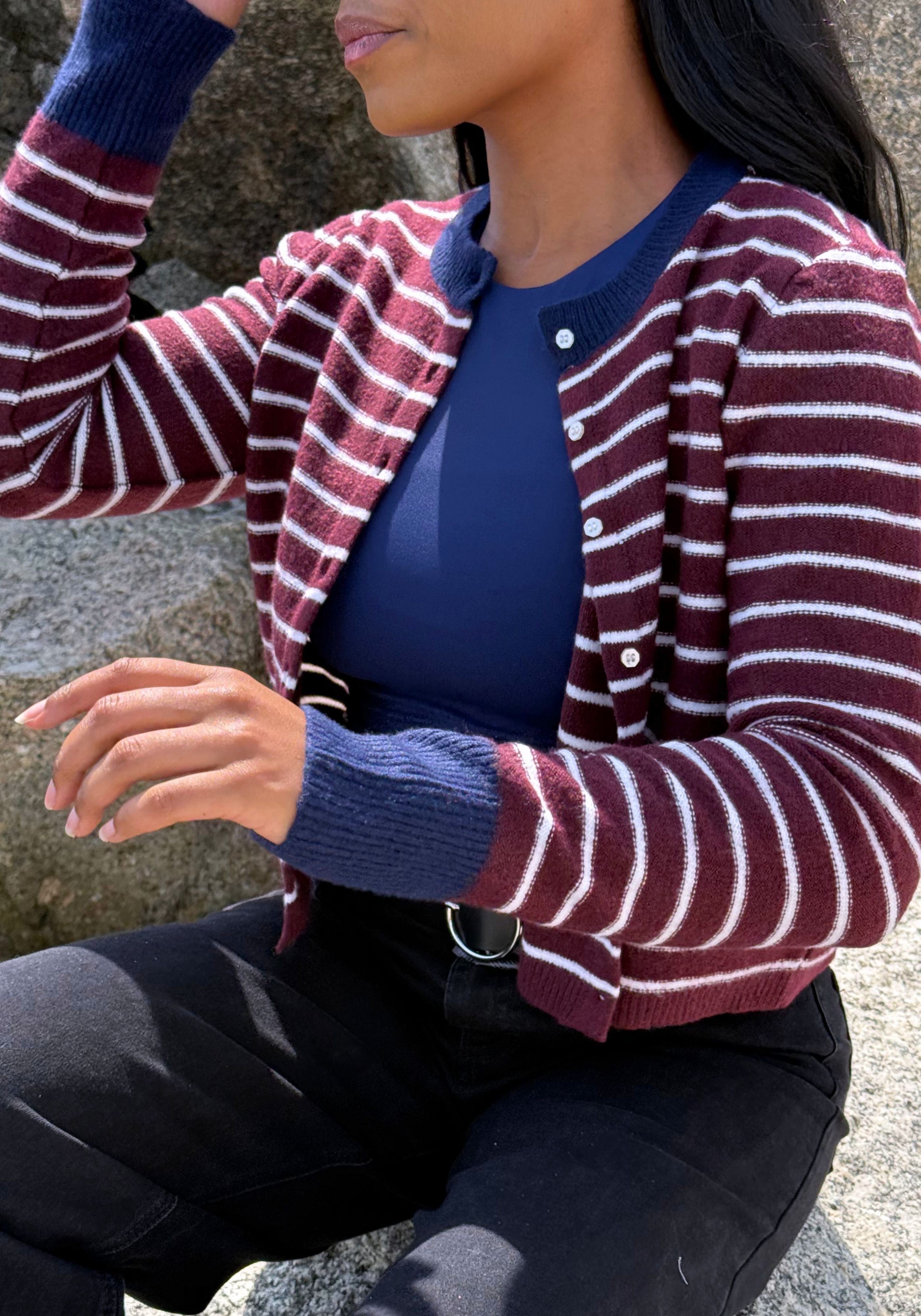 A woman wearing a burgundy and white striped knit cardigan over a navy blue top, paired with black pants.