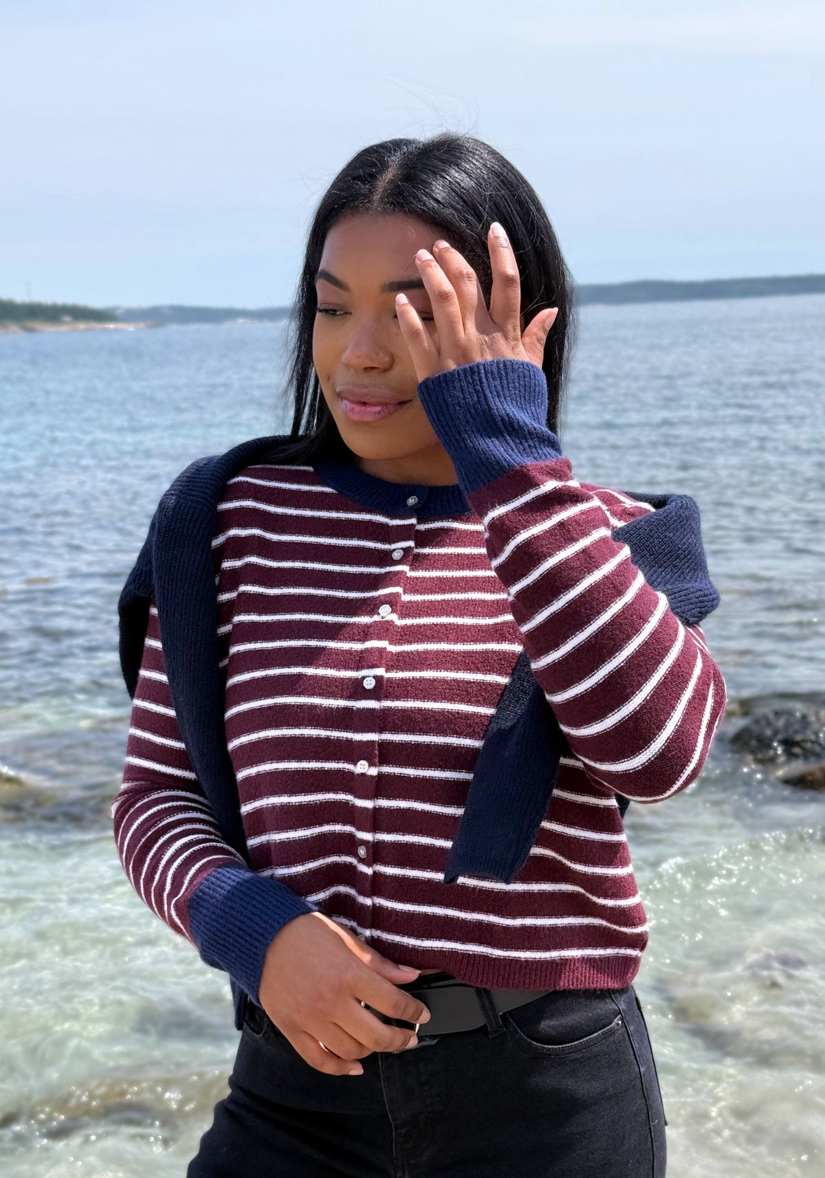 A woman wearing a navy blue and burgundy striped knit cardigan with solid navy sleeves and collar, paired with black pants.