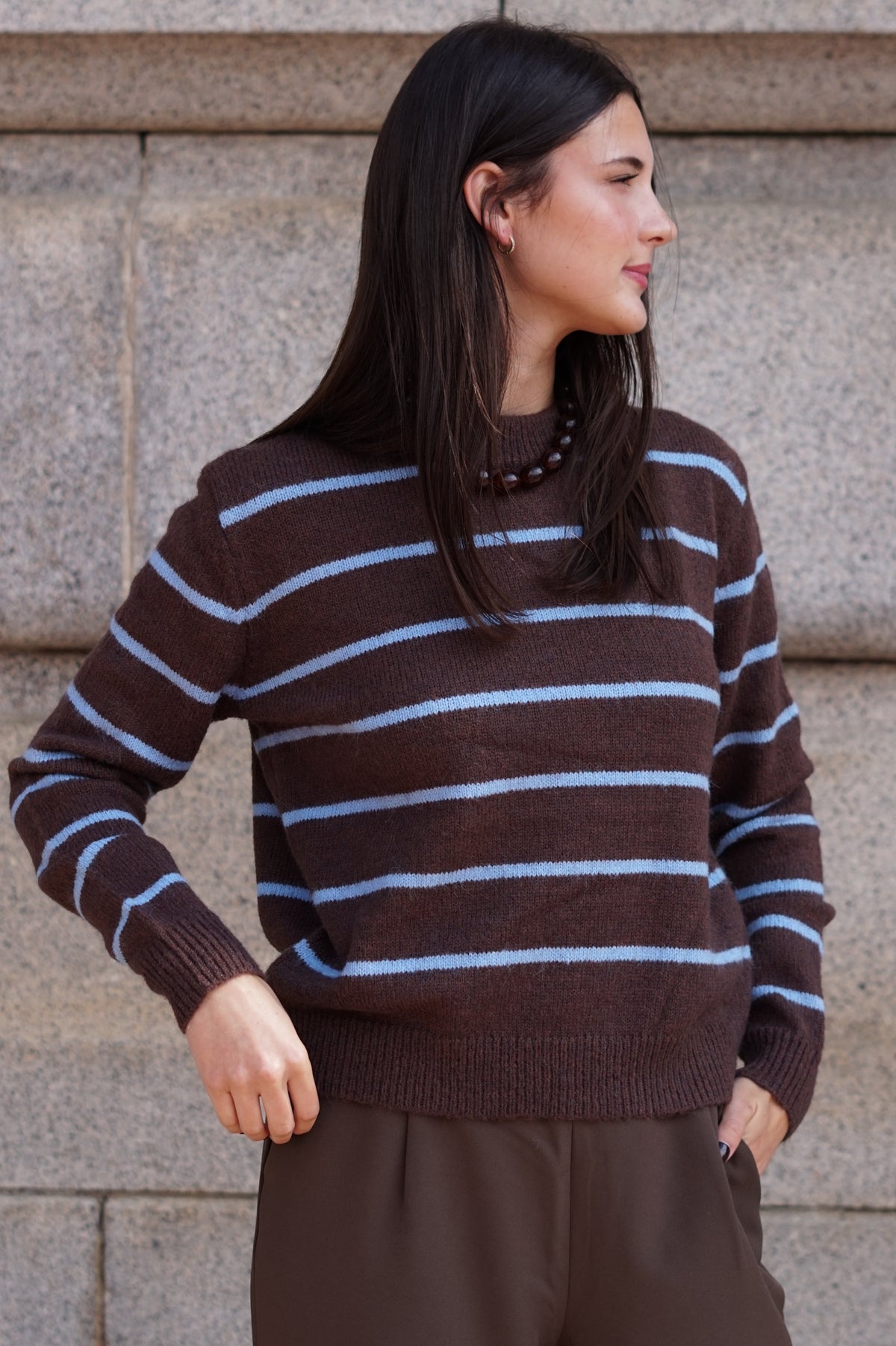 A woman wearing a brown knit sweater with light blue horizontal stripes, paired with brown trousers.
