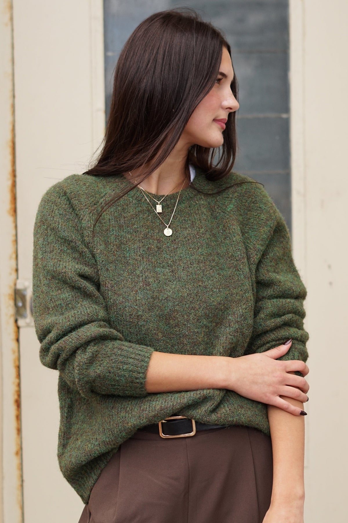 A woman wearing a textured olive green knit sweater and brown trousers