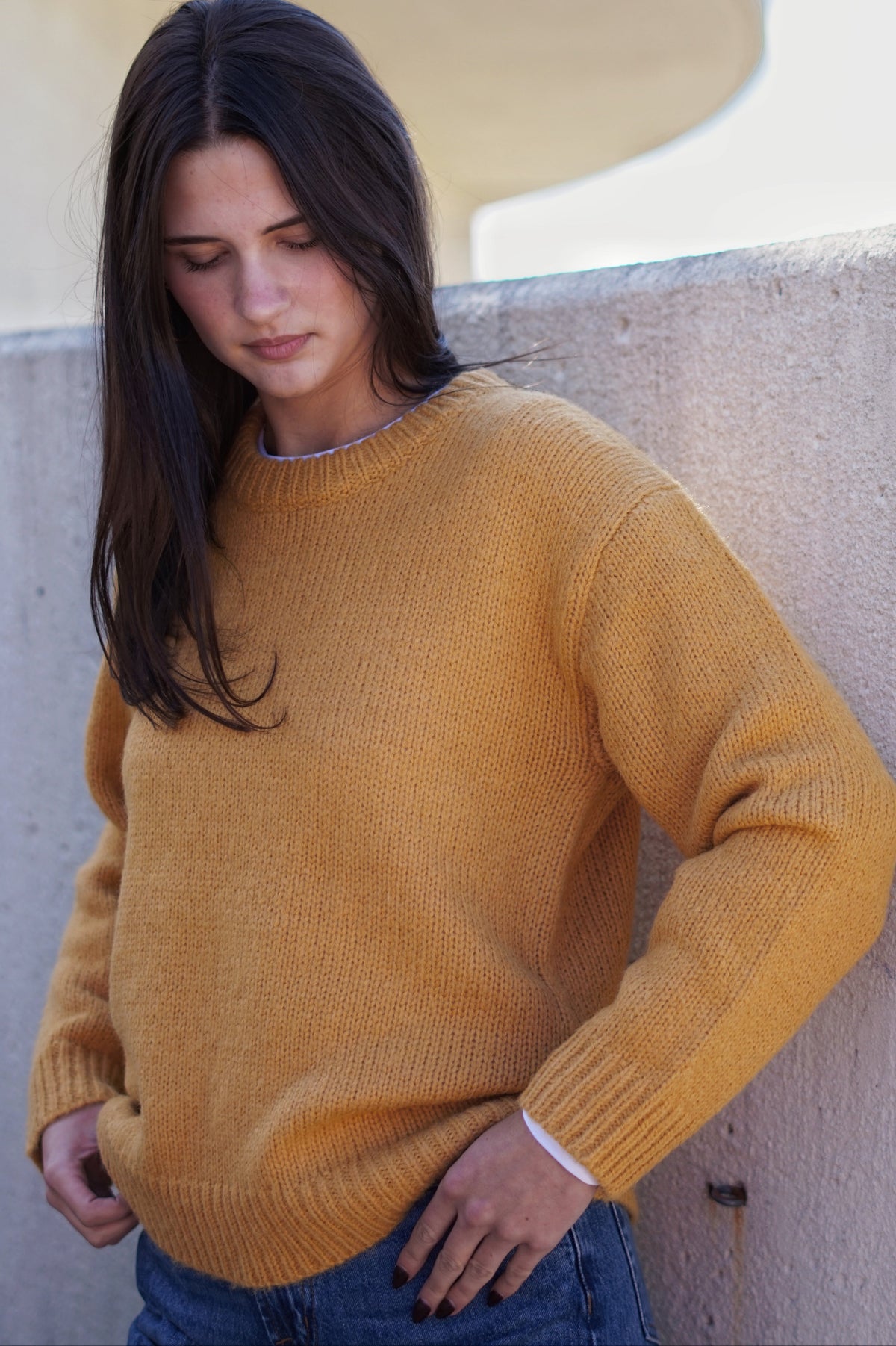A woman wearing a mustard yellow ribbed knit crewneck sweater.