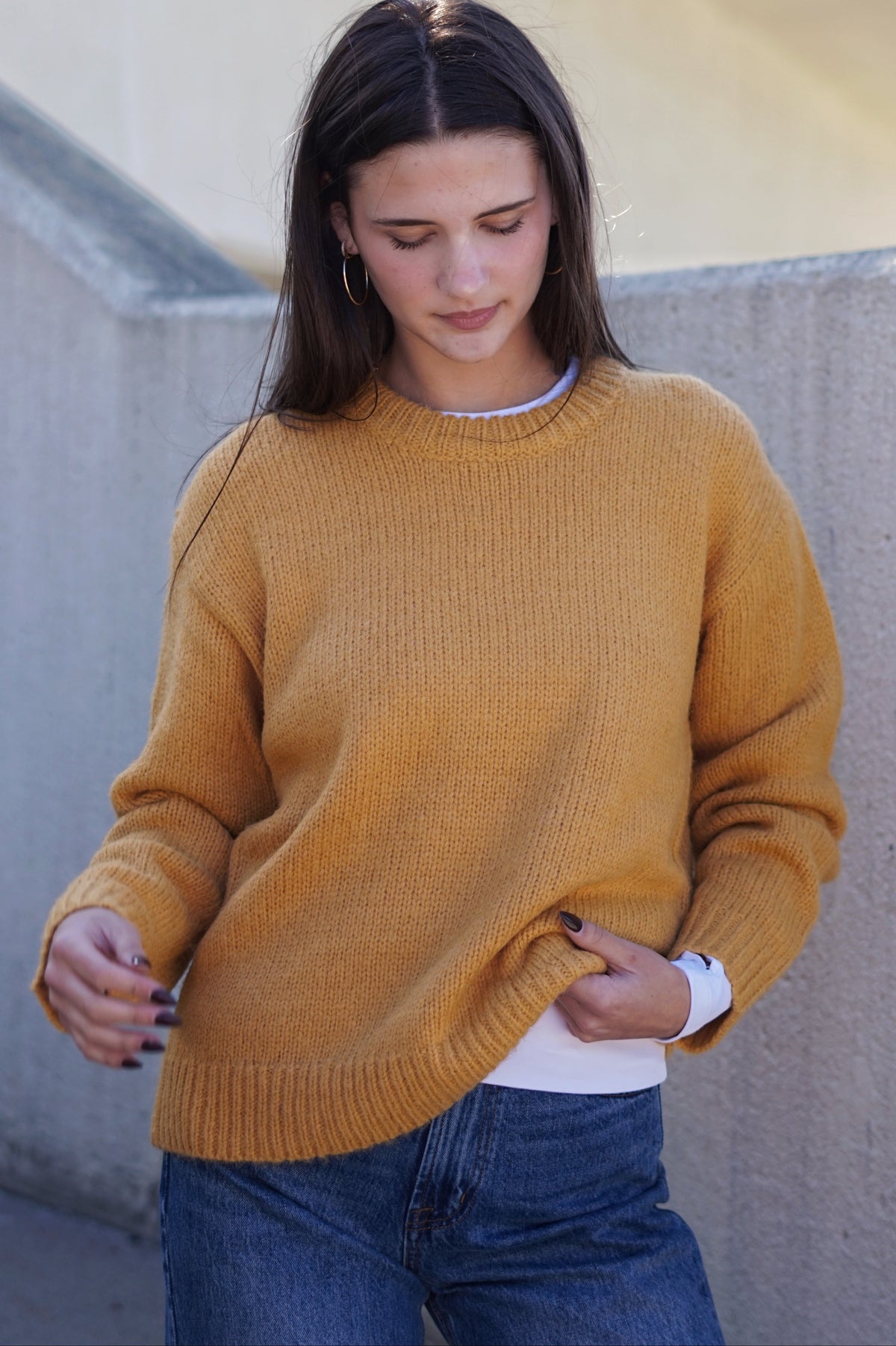 A woman wearing a mustard yellow ribbed knit sweater over a white undershirt and blue jeans