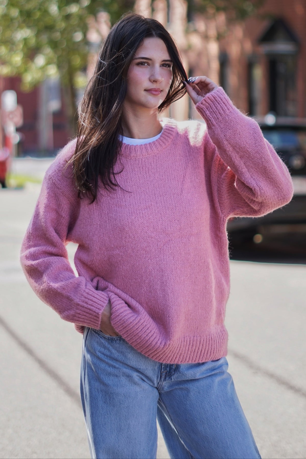 A woman wearing a dusty pink fuzzy knit crewneck sweater and light blue jeans