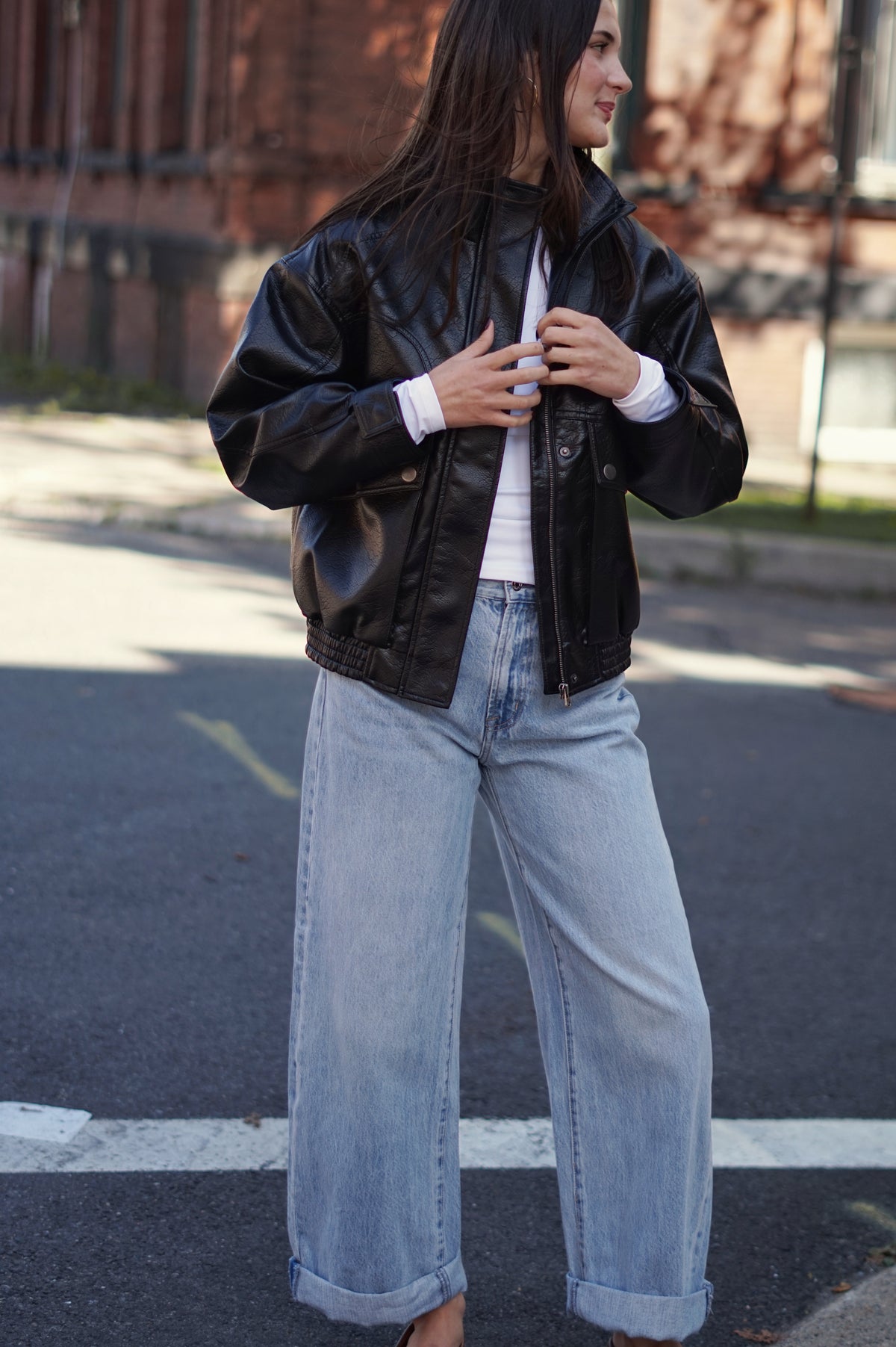 A woman wearing a black faux-leather bomber jacket, light-wash wide-leg jeans, and a white t-shirt,