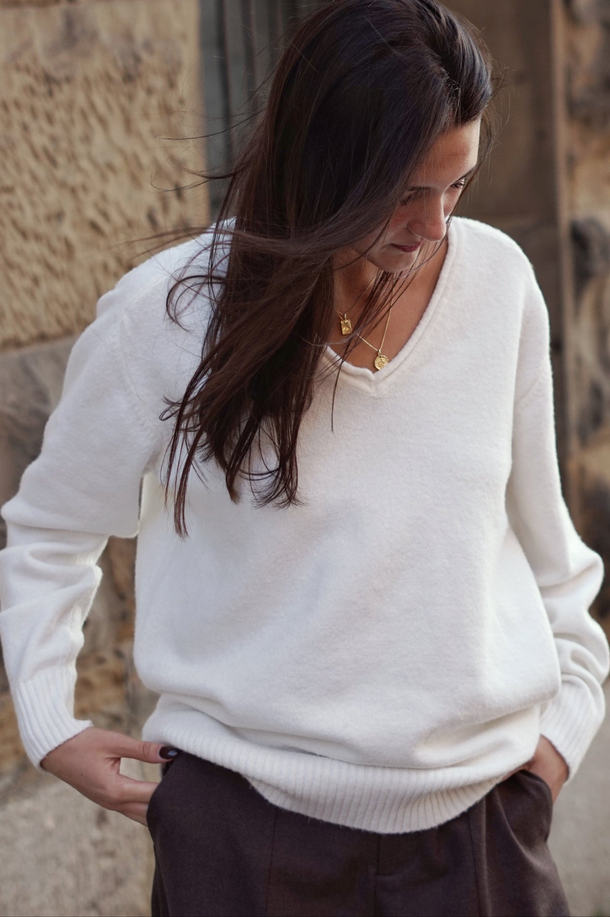 A woman wearing a white knit V-neck sweater and dark brown trousers