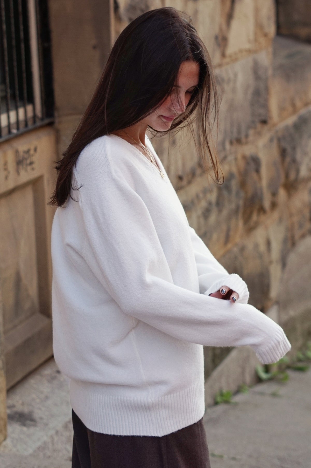 A woman wearing a loose white knit sweater and a dark brown skirt.