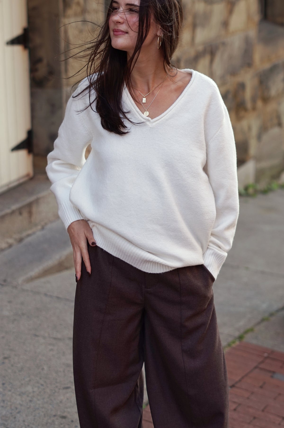 A woman wearing an oversized cream-colored knit V-neck sweater and dark brown wide-leg trousers,