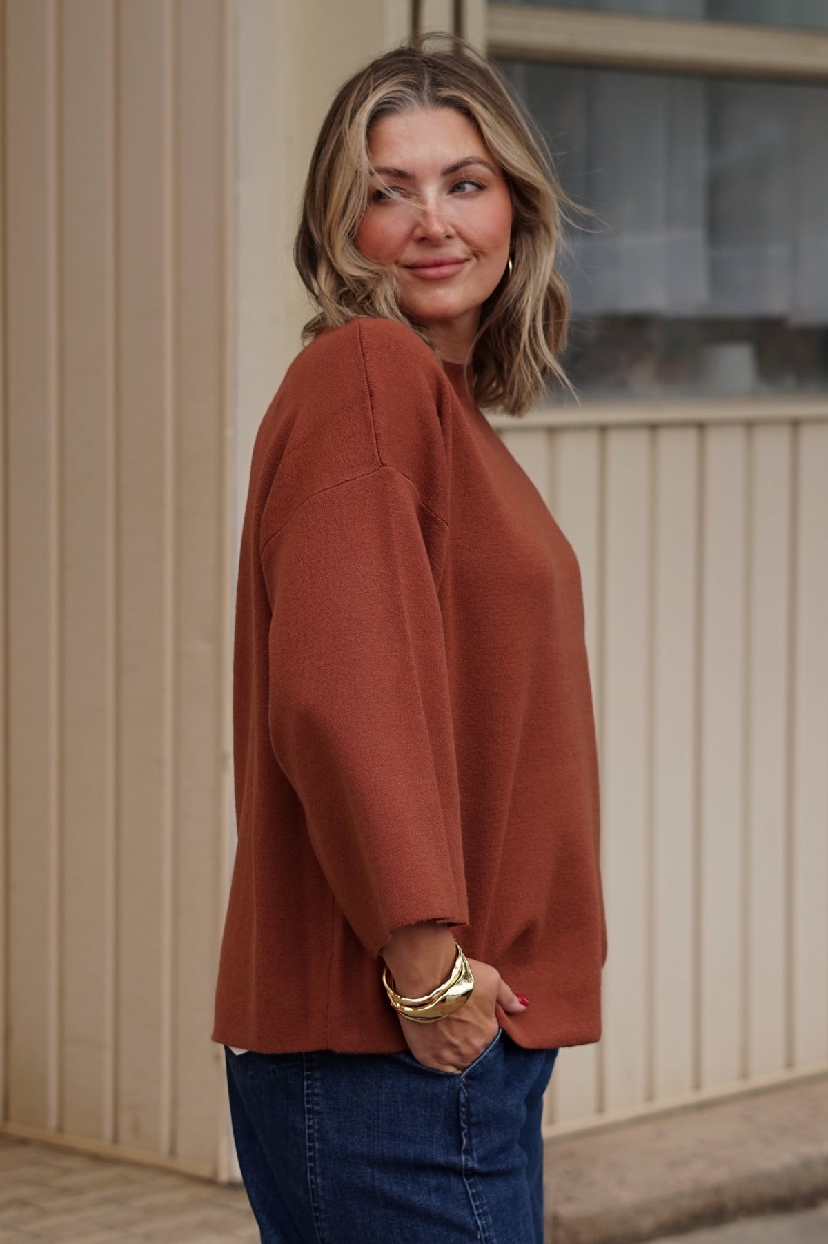 A woman wearing a rust-colored knit sweater and blue jeans 