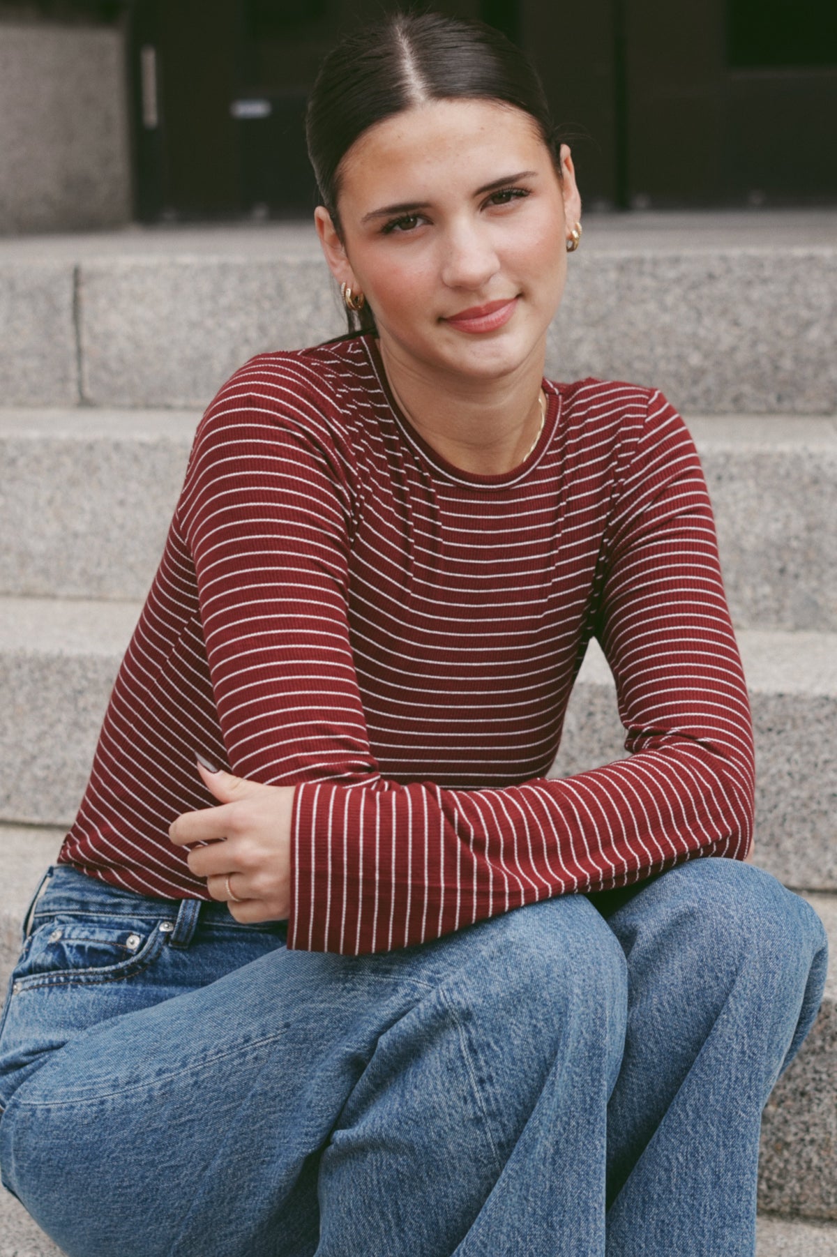 A woman wearing a long-sleeve crewneck top with thin red and white horizontal stripes, paired with blue jeans.