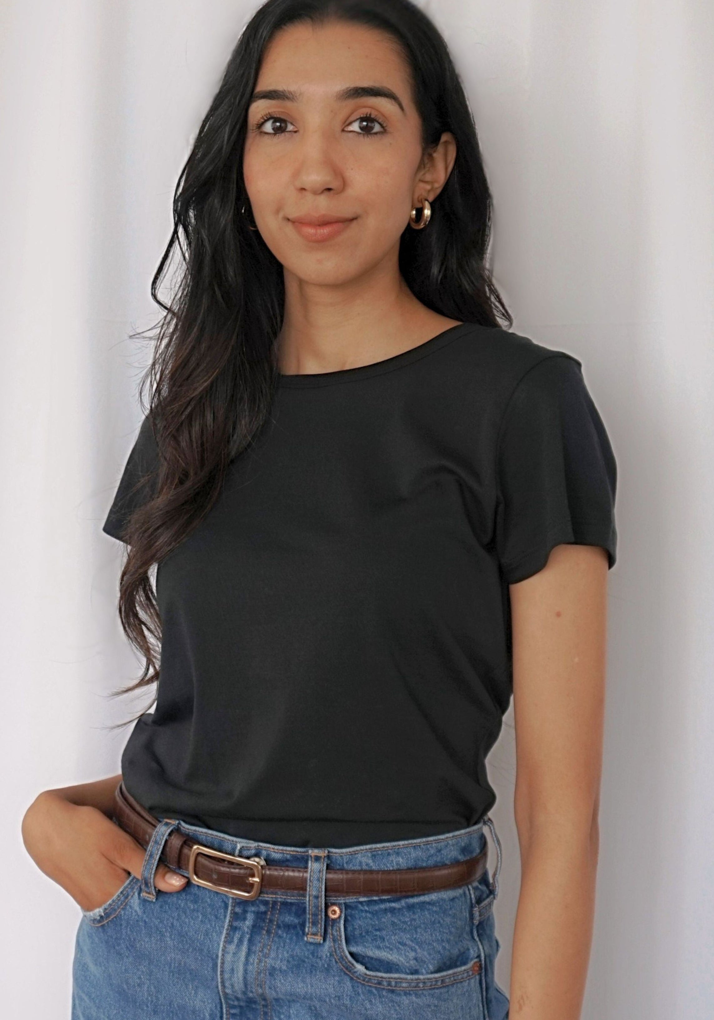 A woman wearing a black short-sleeve crewneck t-shirt and blue jeans with a brown belt.