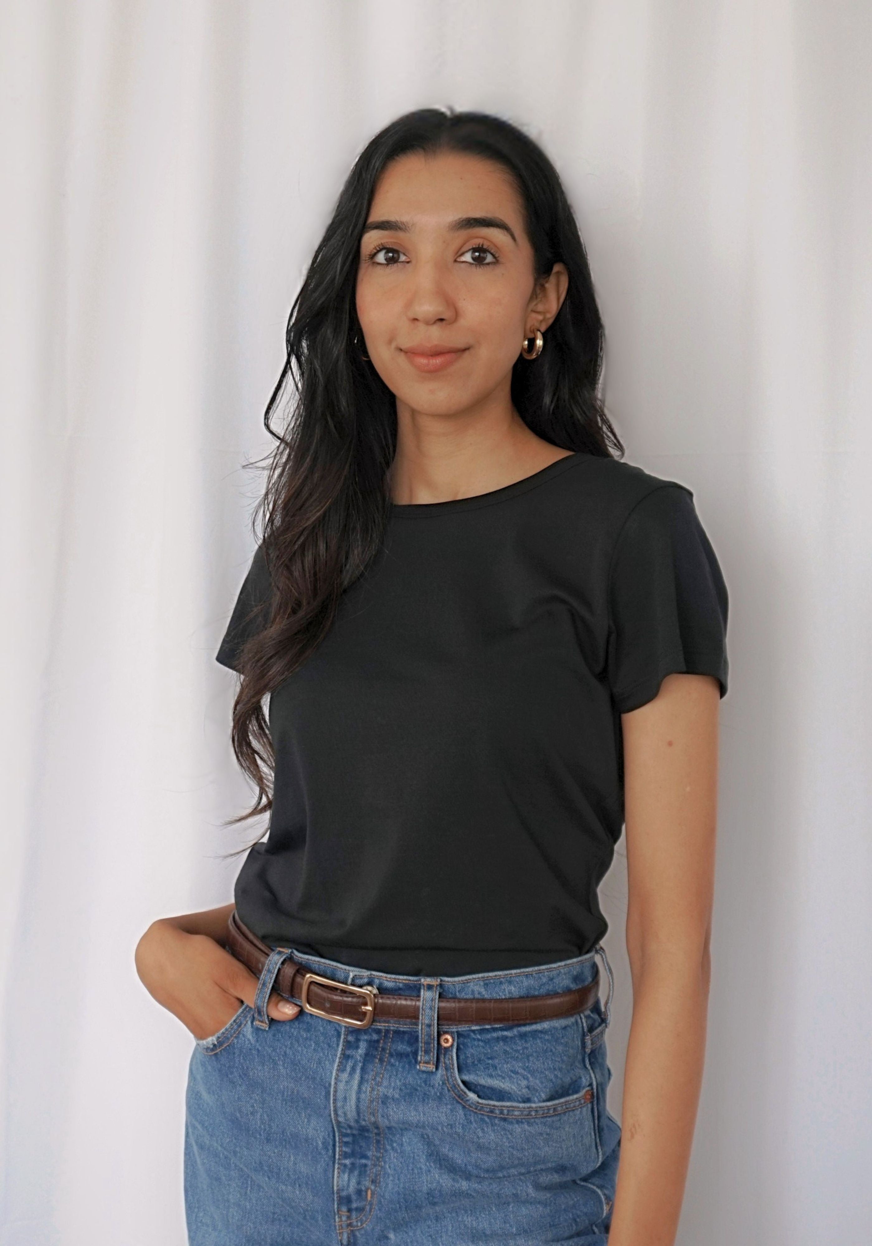 A woman wearing a black short-sleeve crewneck t-shirt and blue jeans with a brown belt.