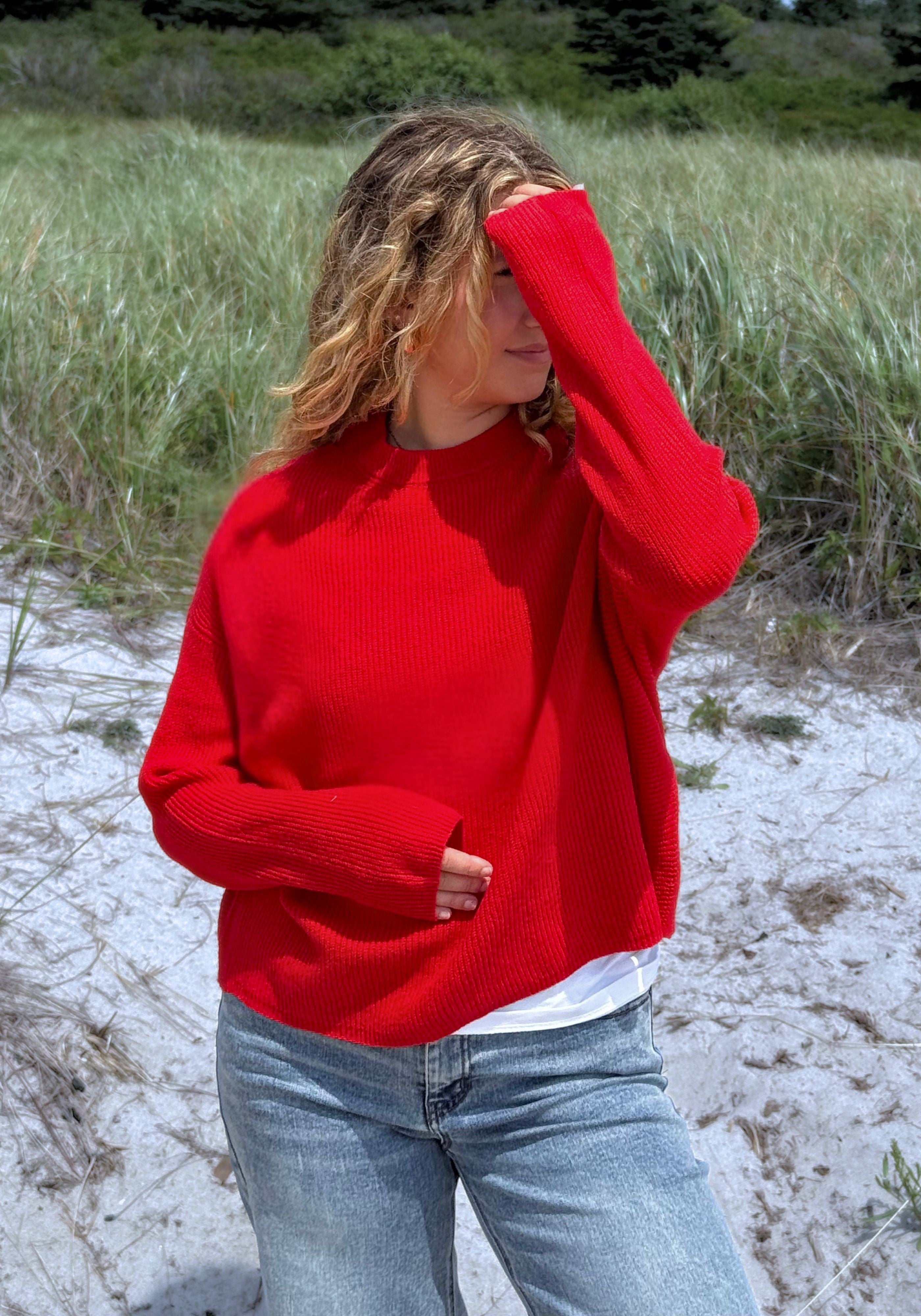 A woman wearing a bright red knit sweater and light blue jeans.