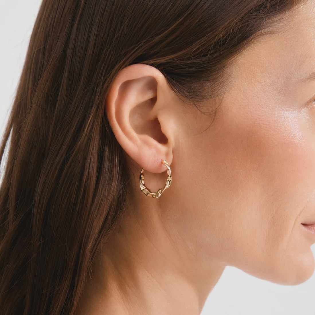 Close-up of a person wearing a gold hoop earring with a plain background